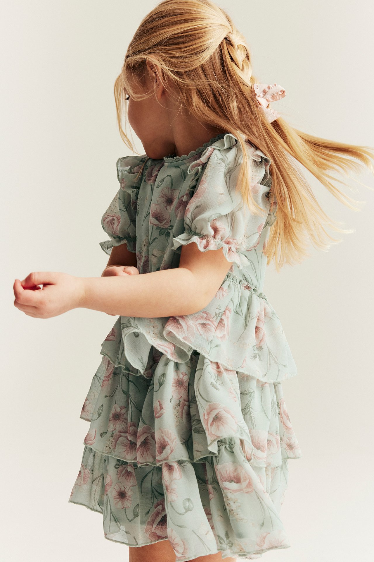 Back view of a kid wearing a light green floral tiered chiffon dress and a pink hair bow.