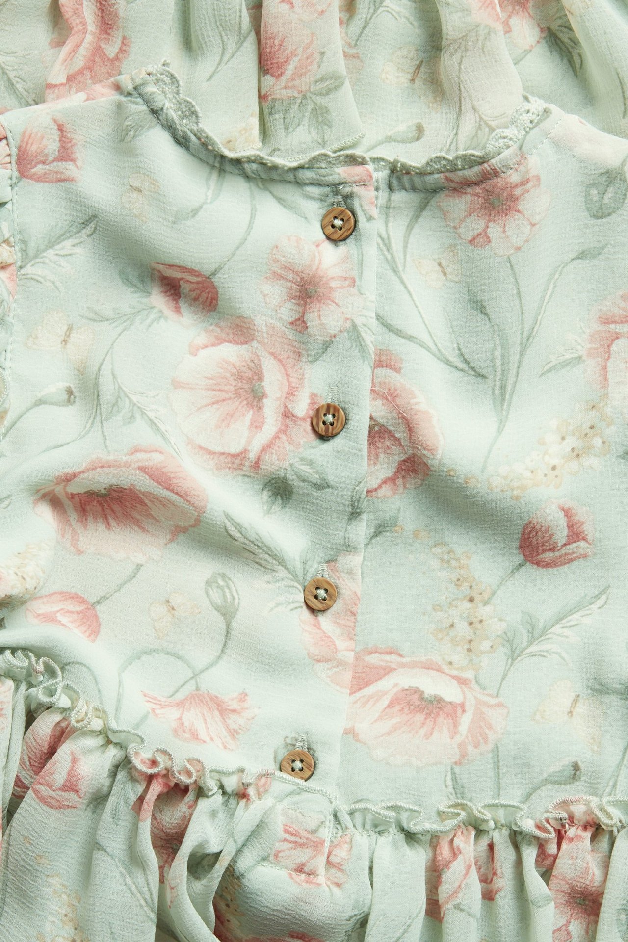 Close-up of a light green floral chiffon dress with ruffles and wooden buttons.