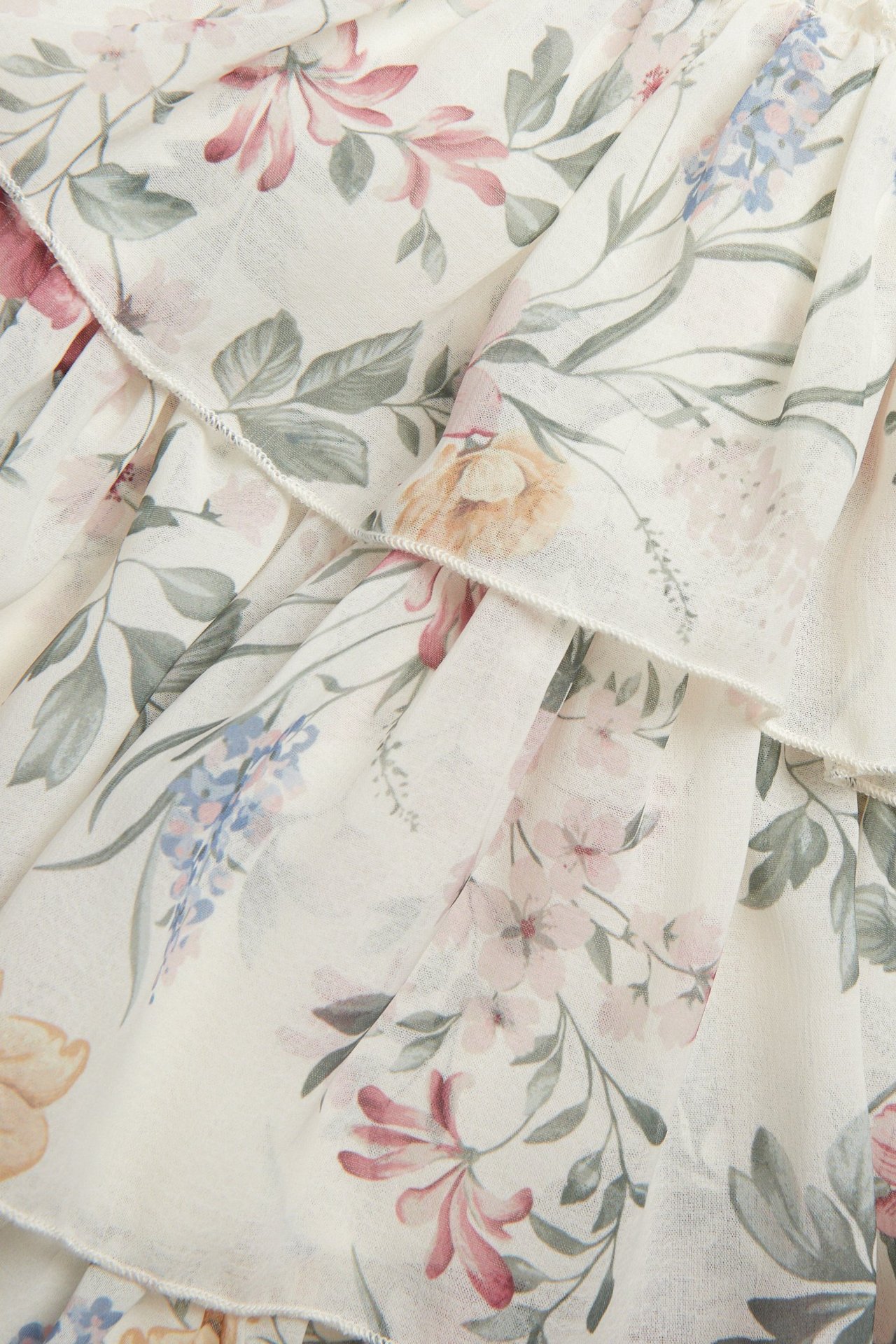 Nahaufnahme eines cremefarbenen floralen Chiffonkleides mit Rüschen und farbenfrohem Muster.