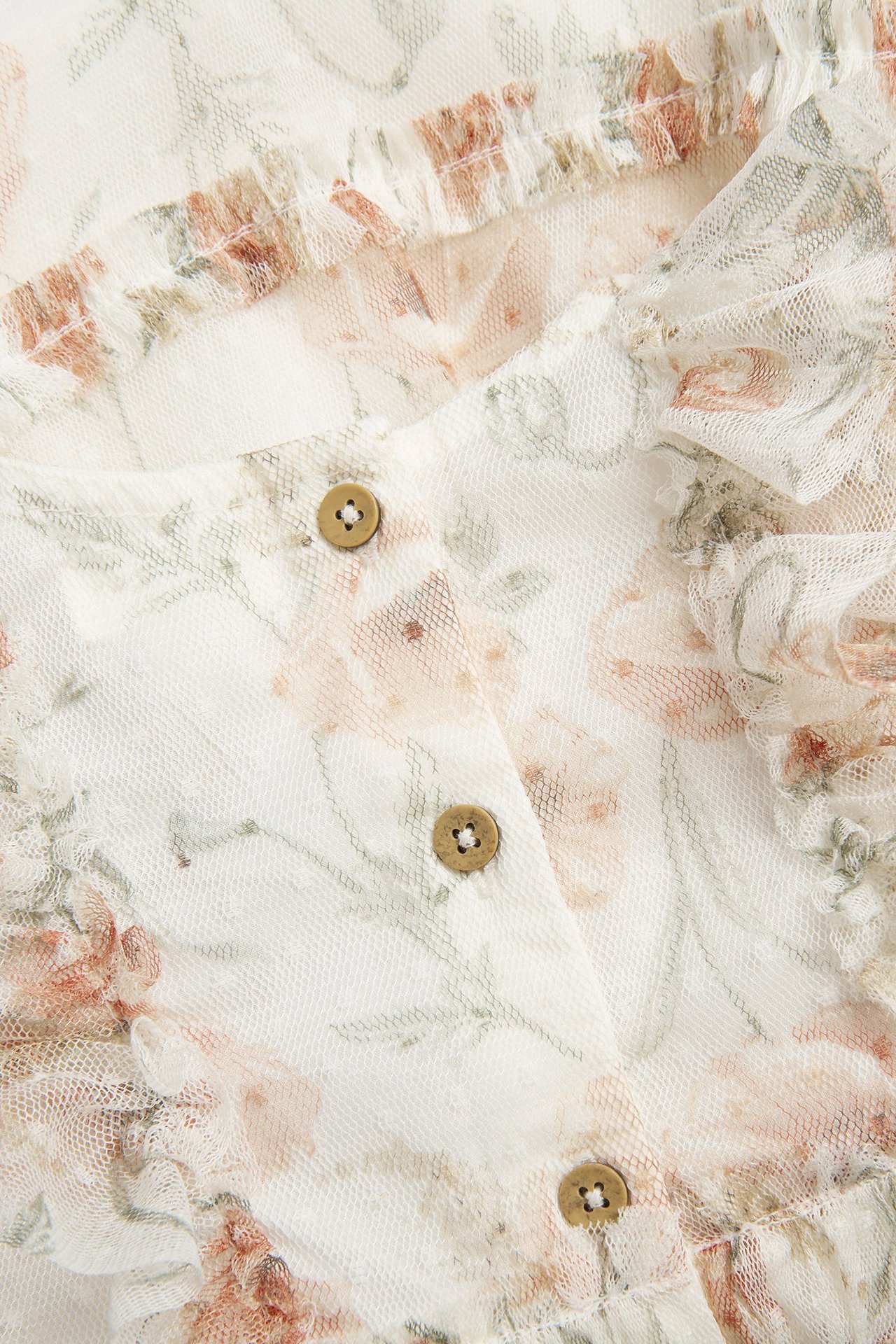 Nahaufnahme eines cremefarbenen floralen Netz-Kleides mit Punktstruktur, Rüschen und Holzknöpfen.