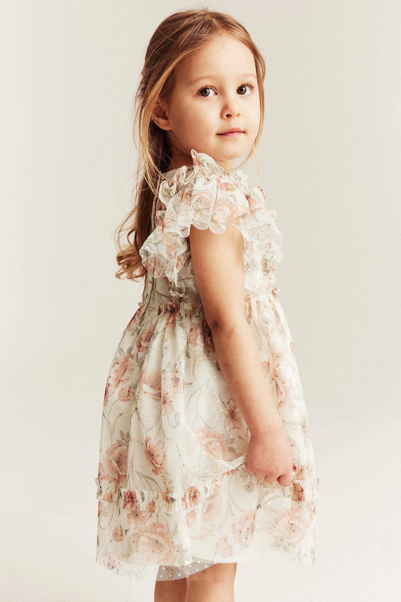 Seitenansicht eines Kindes in off-weißem Blumen-Mesh-Kleid mit Rüschenärmeln und Punktstruktur.