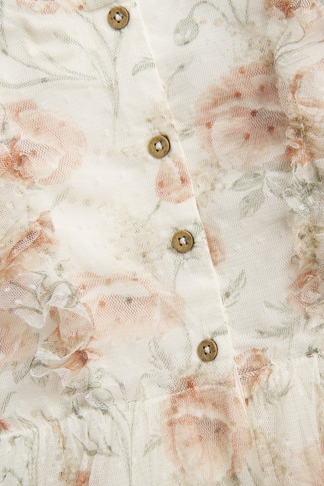 Nahaufnahme eines cremeweißen Blumen-Meshkleides mit Punktstruktur, einer Rüsche und braunen Knöpfen.