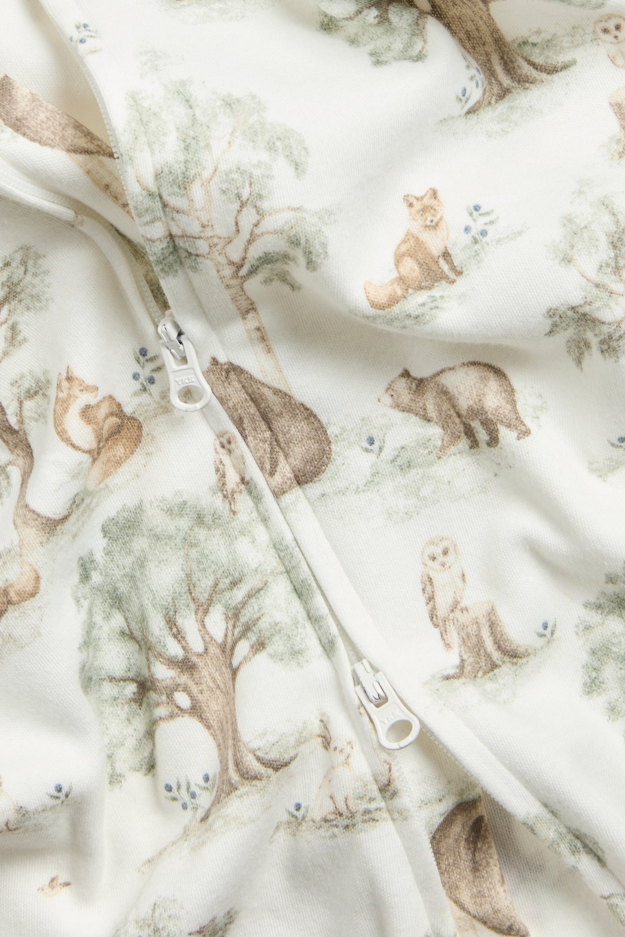 Close-up of an offwhite cotton baby romper with a forest animal print and a front two-way zipper.