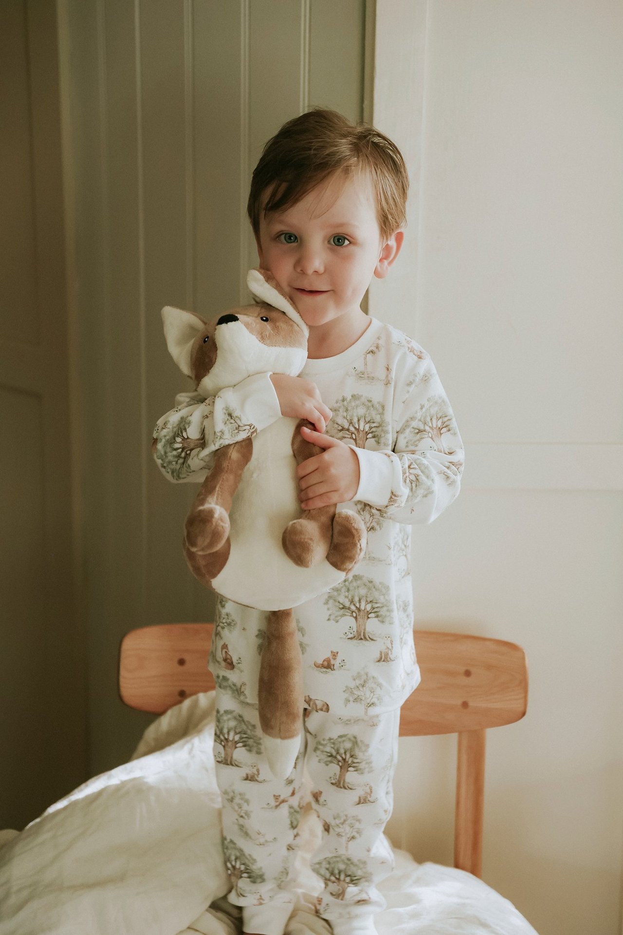 Vorderansicht eines Kindes in cremeweißem Baumwollpyjama mit Waldmotiv, hält einen Plüschfuchs.