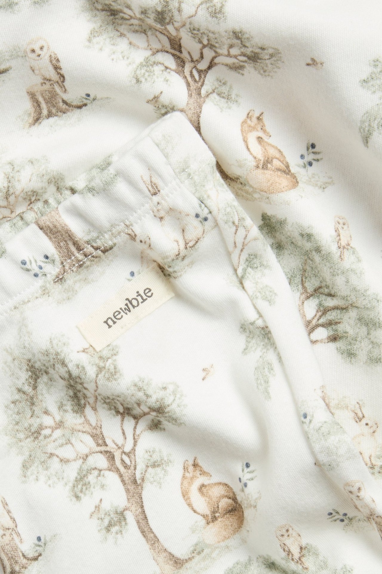 Close-up of off-white cotton pajamas with a detailed forest animal print and a 'newbie' label.