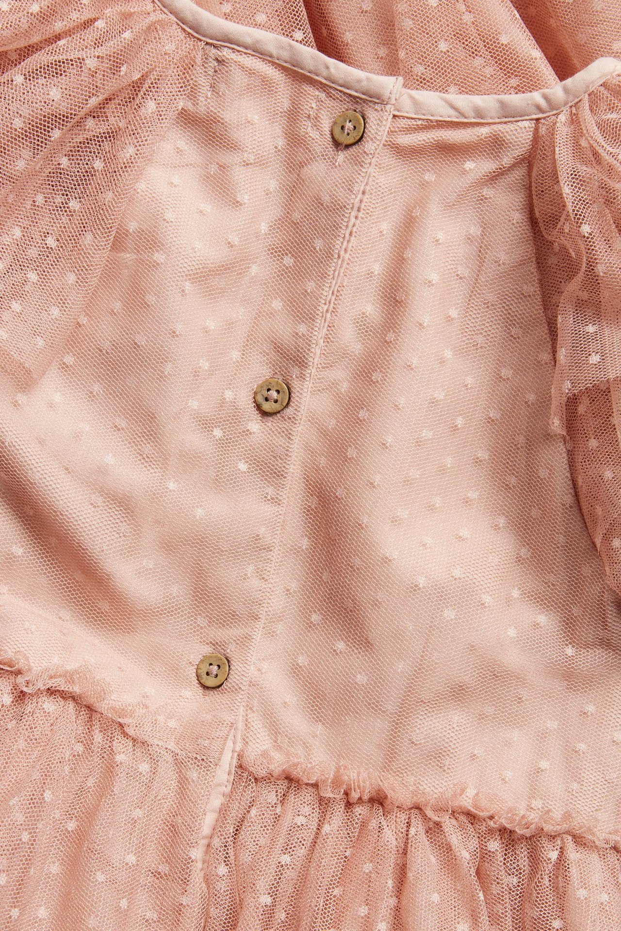 Close-up back view of a pink dotted mesh dress with three wooden buttons and ruffles.