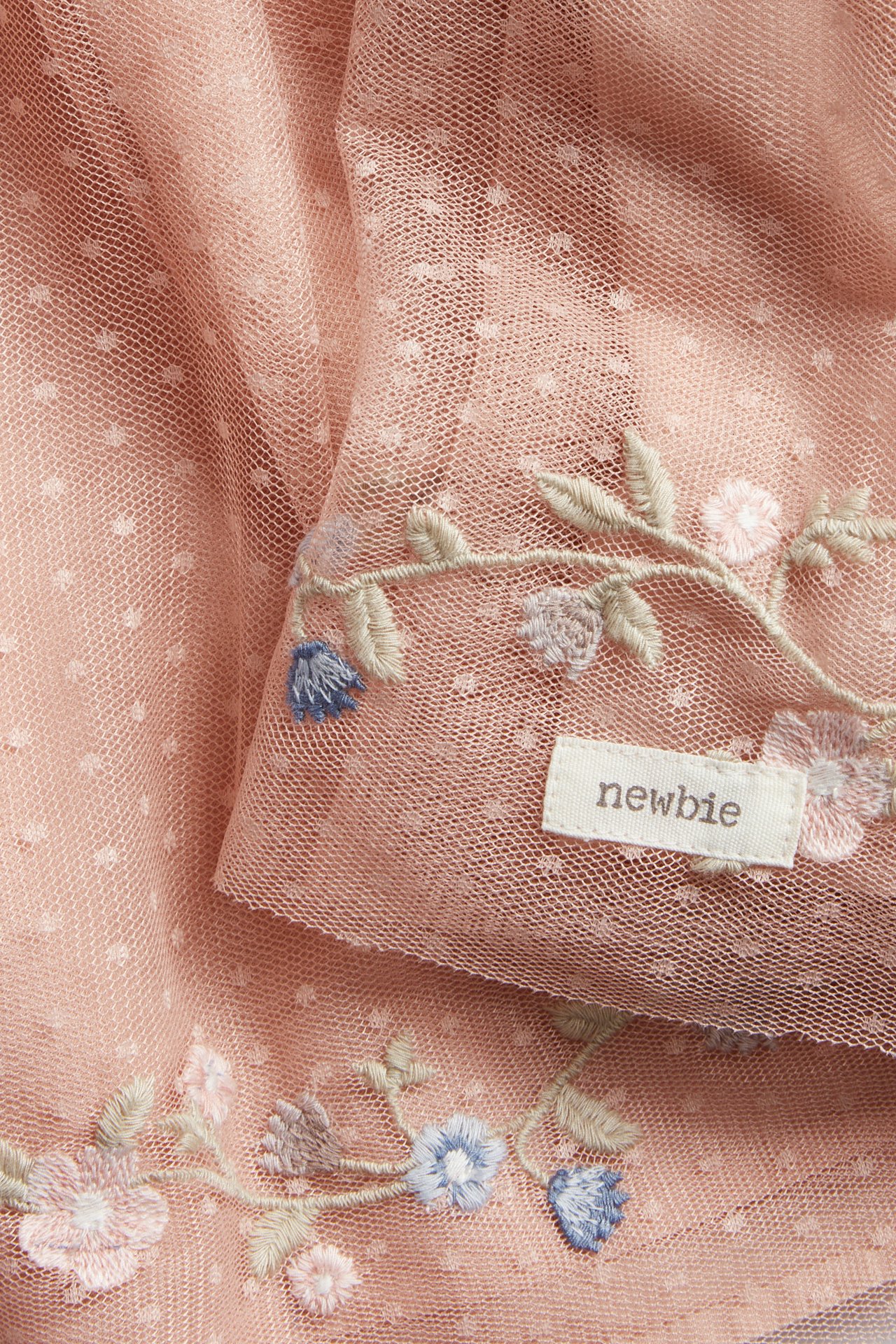 Close-up of a pink dotted mesh dress featuring colorful floral embroidery and a Newbie brand tag.