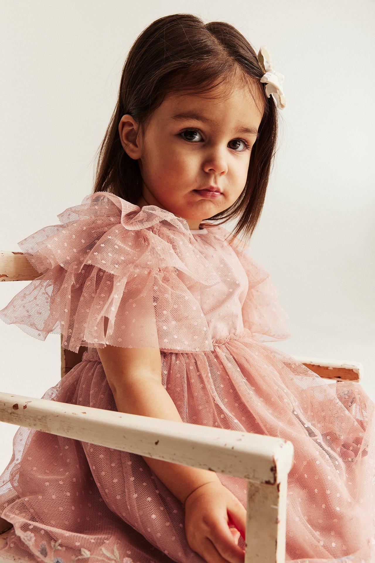 Close-up of a kid wearing a pink polka dot mesh dress with tiered ruffle sleeves and white hair clip.