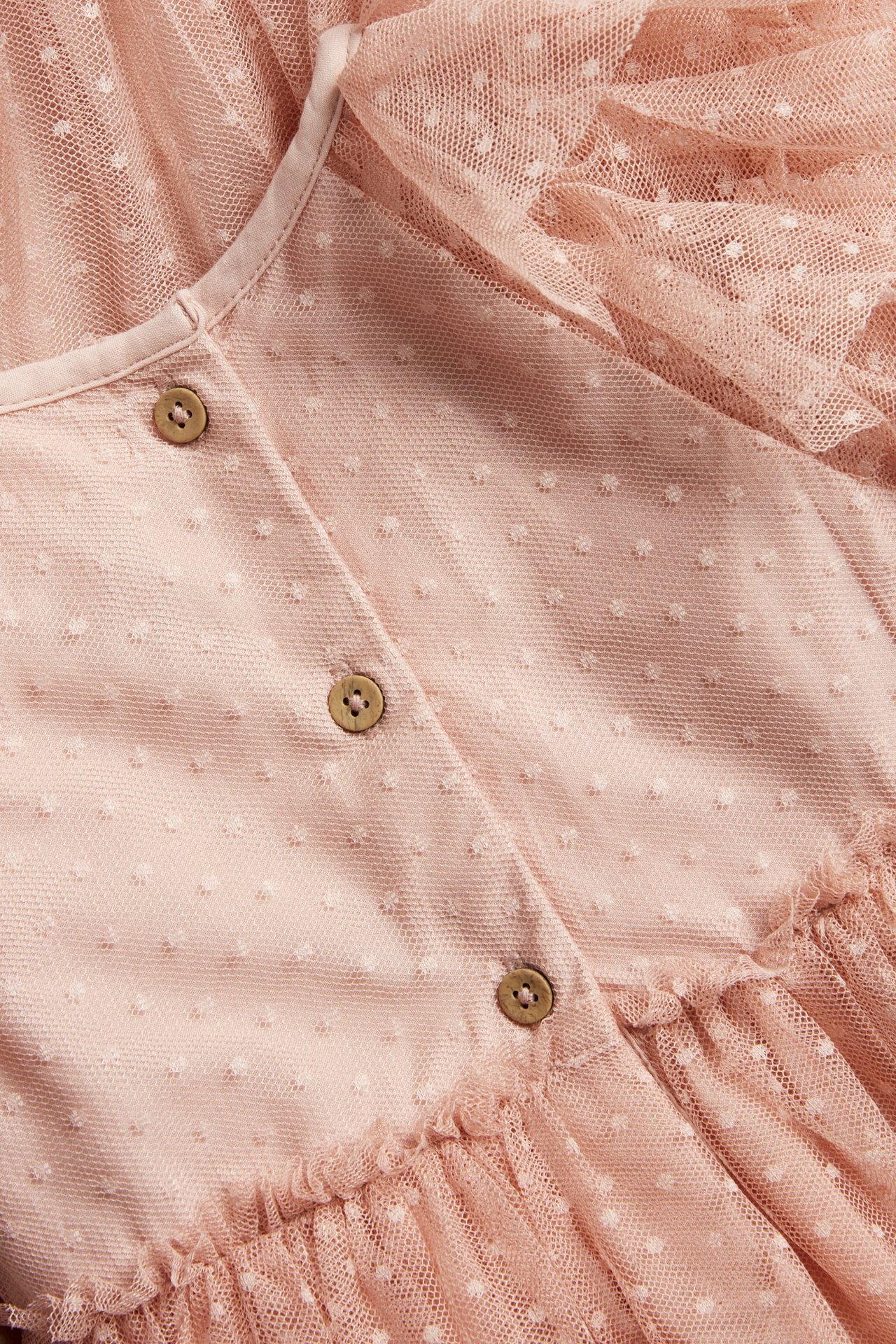 Nahaufnahme eines rosa Kinder-Meshkleides mit weißen Punkten, Holzknöpfen und Rüschen.