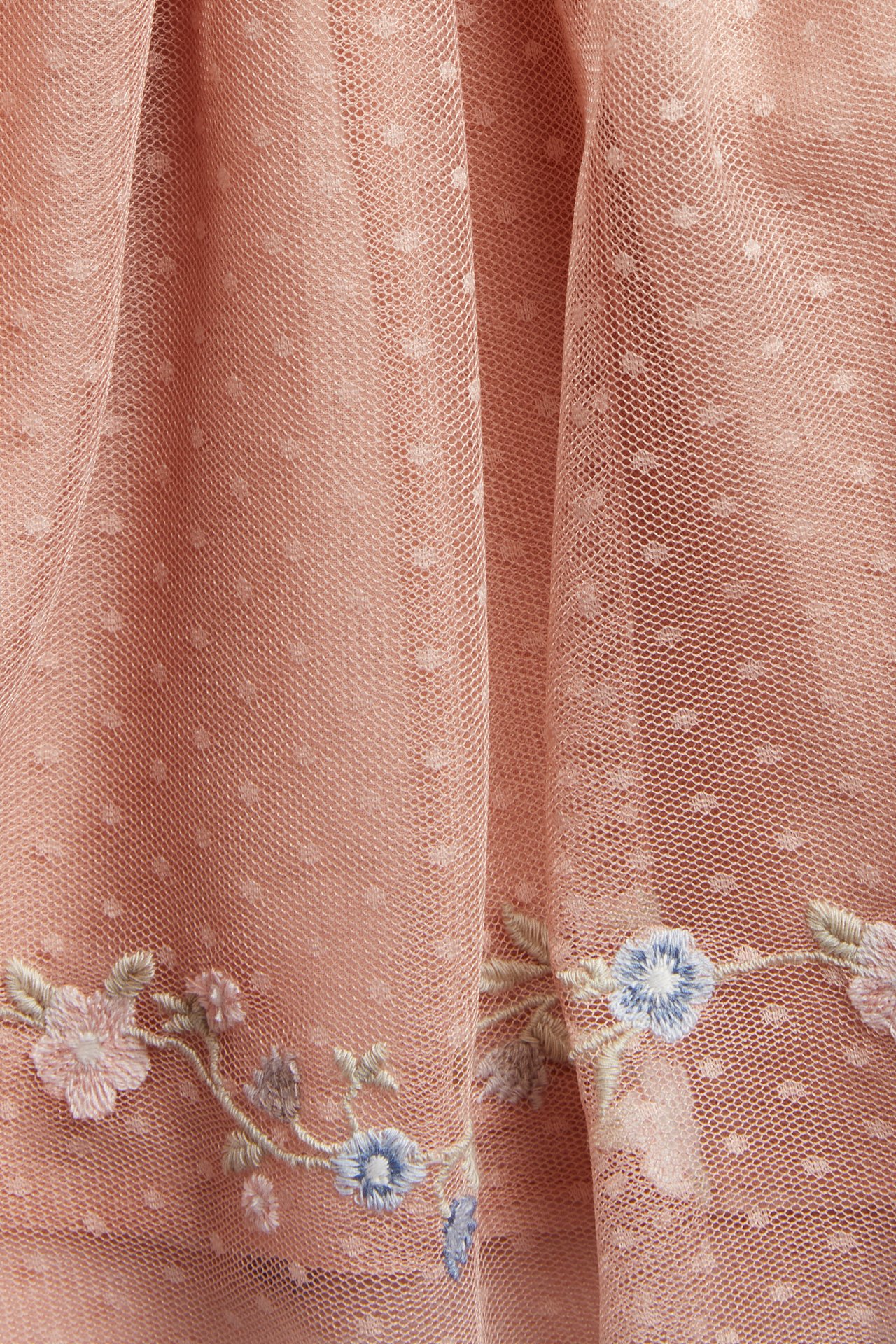 Close-up of a pink dotted mesh dress with blue and pink floral embroidery at the hem.