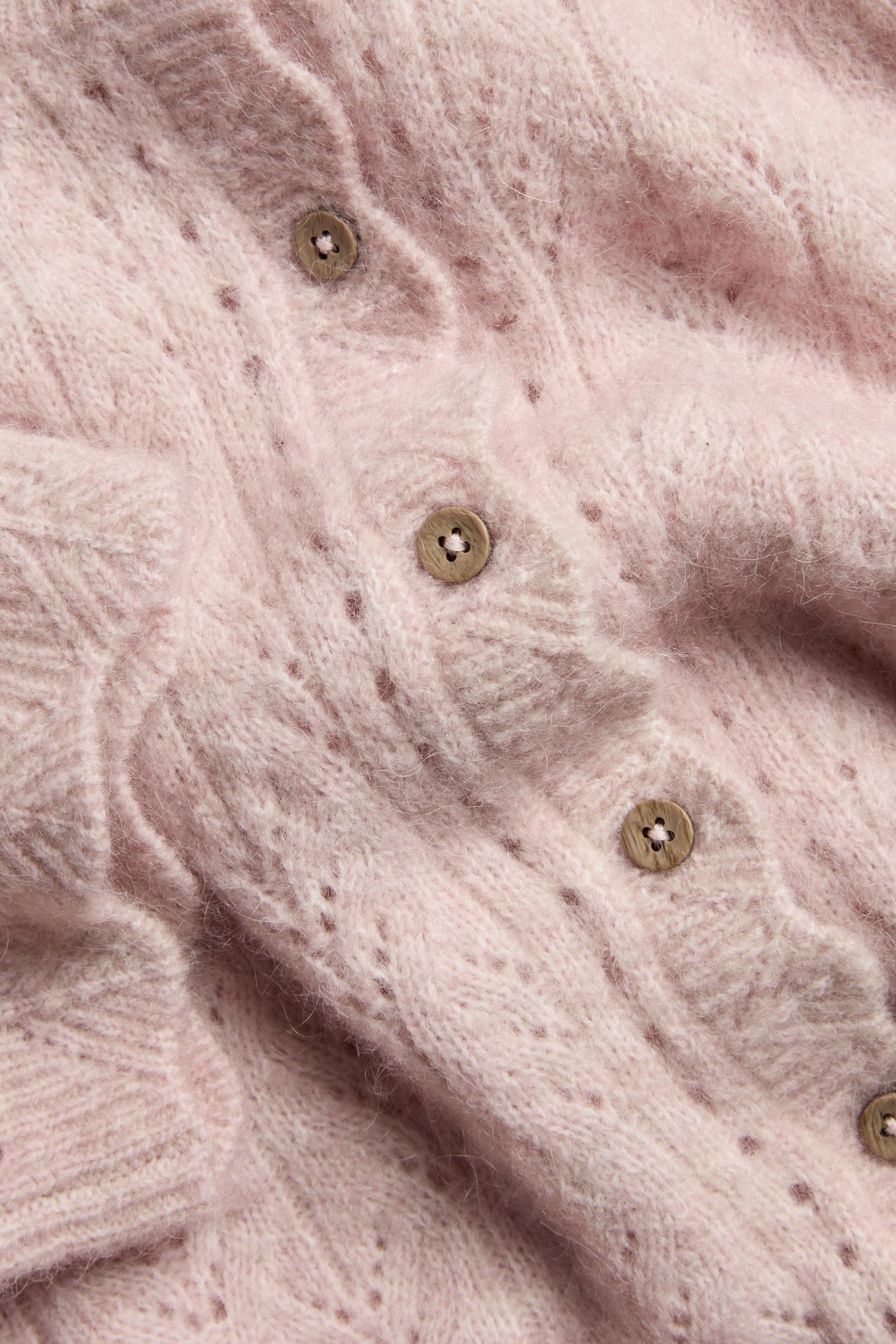 Nahaufnahme: Rosa Wollmisch-Strickjacke mit Ajourmuster und Holzknöpfen.