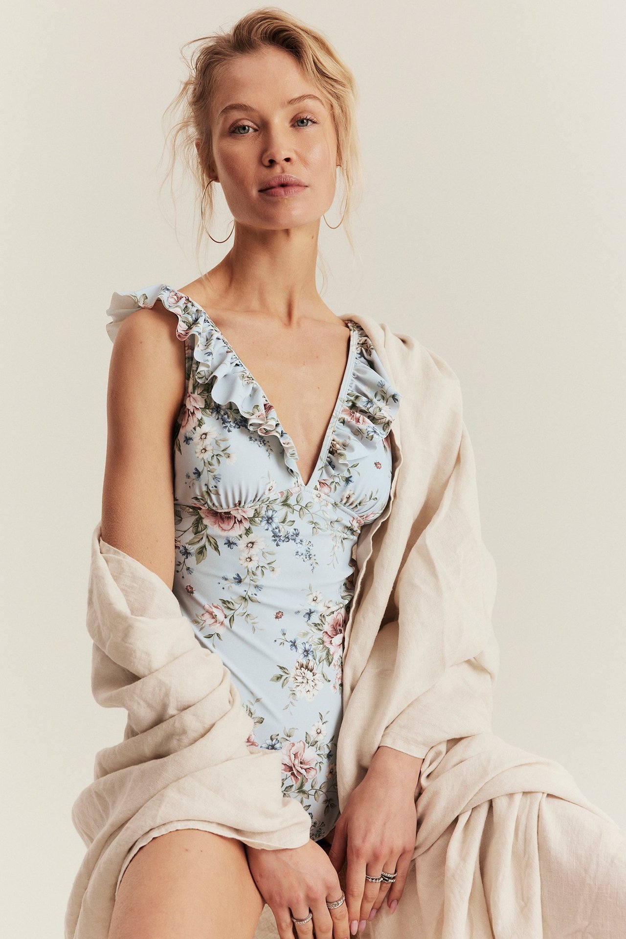 Front view of a woman in a light blue floral ruffled swimsuit with a beige linen shawl.
