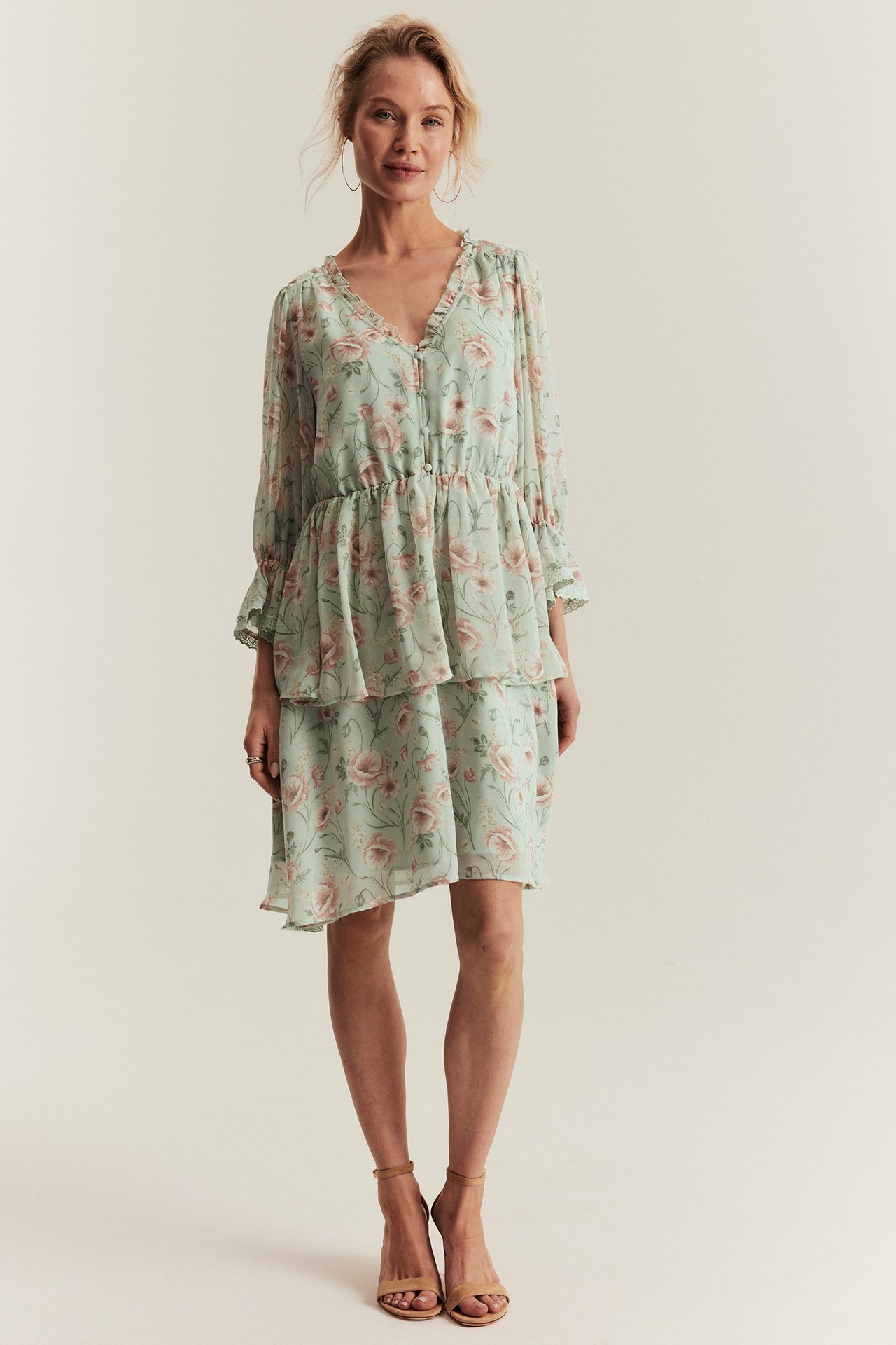 Front view: Woman in light green floral chiffon dress with ruffles, buttons, and nude sandals.