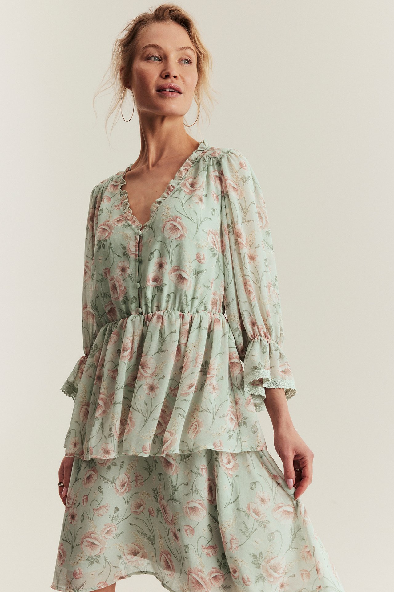 Front view of a woman wearing a light green floral chiffon dress with ruffles, covered buttons, and tiered skirt.