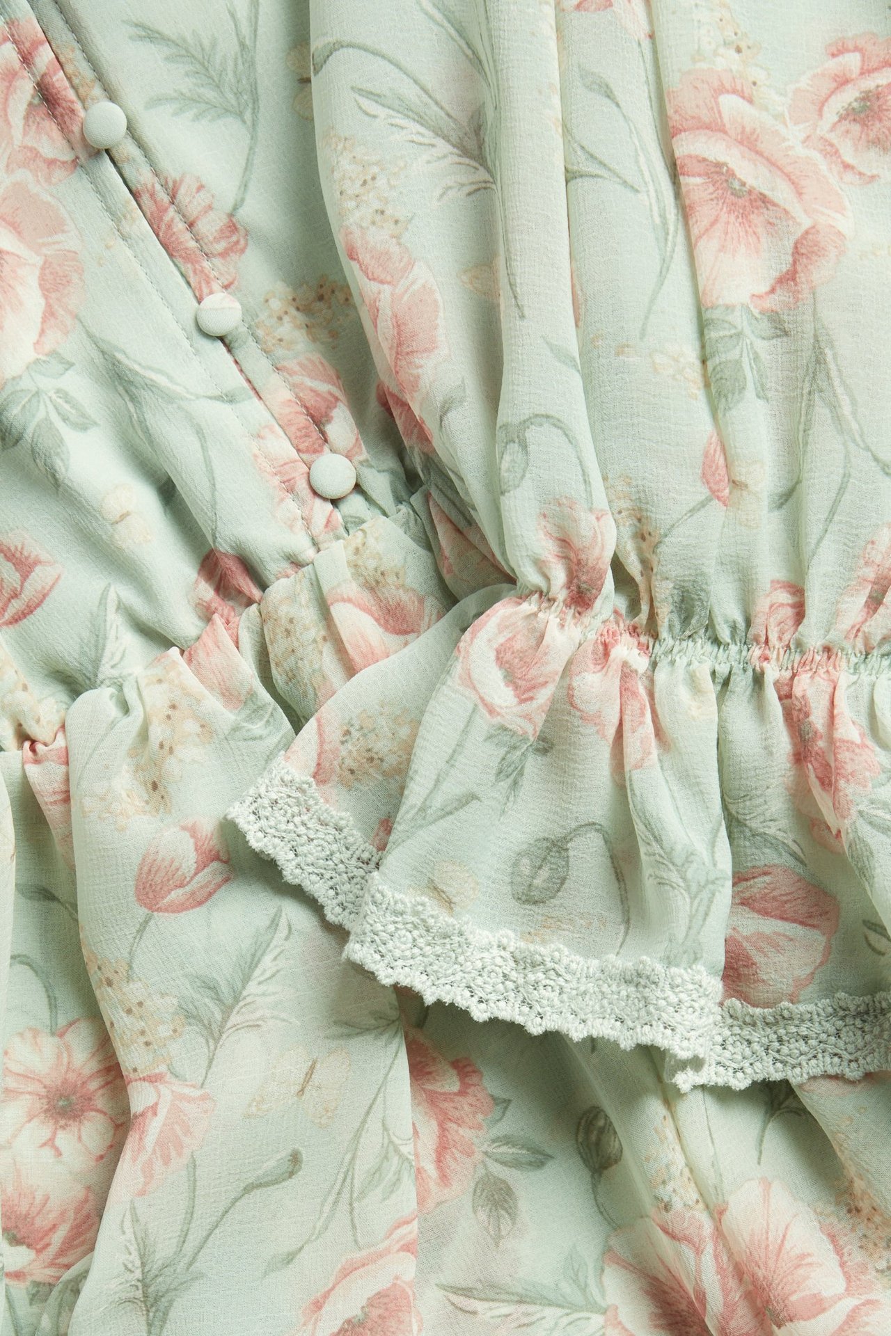 Close-up of a light green floral chiffon woman's dress with covered buttons, ruffles, and elastic.