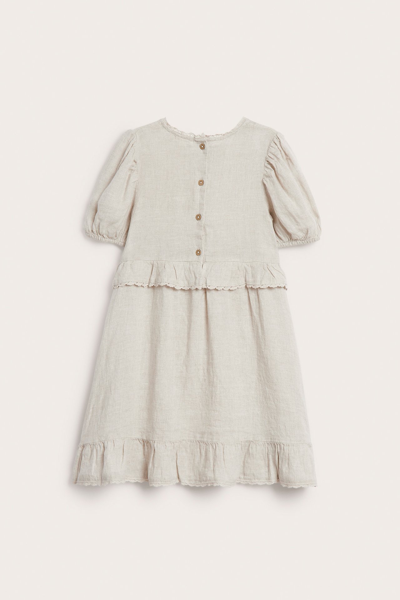 Back view of a kid's light beige linen dress with puff sleeves, ruffles, buttons, and lace.