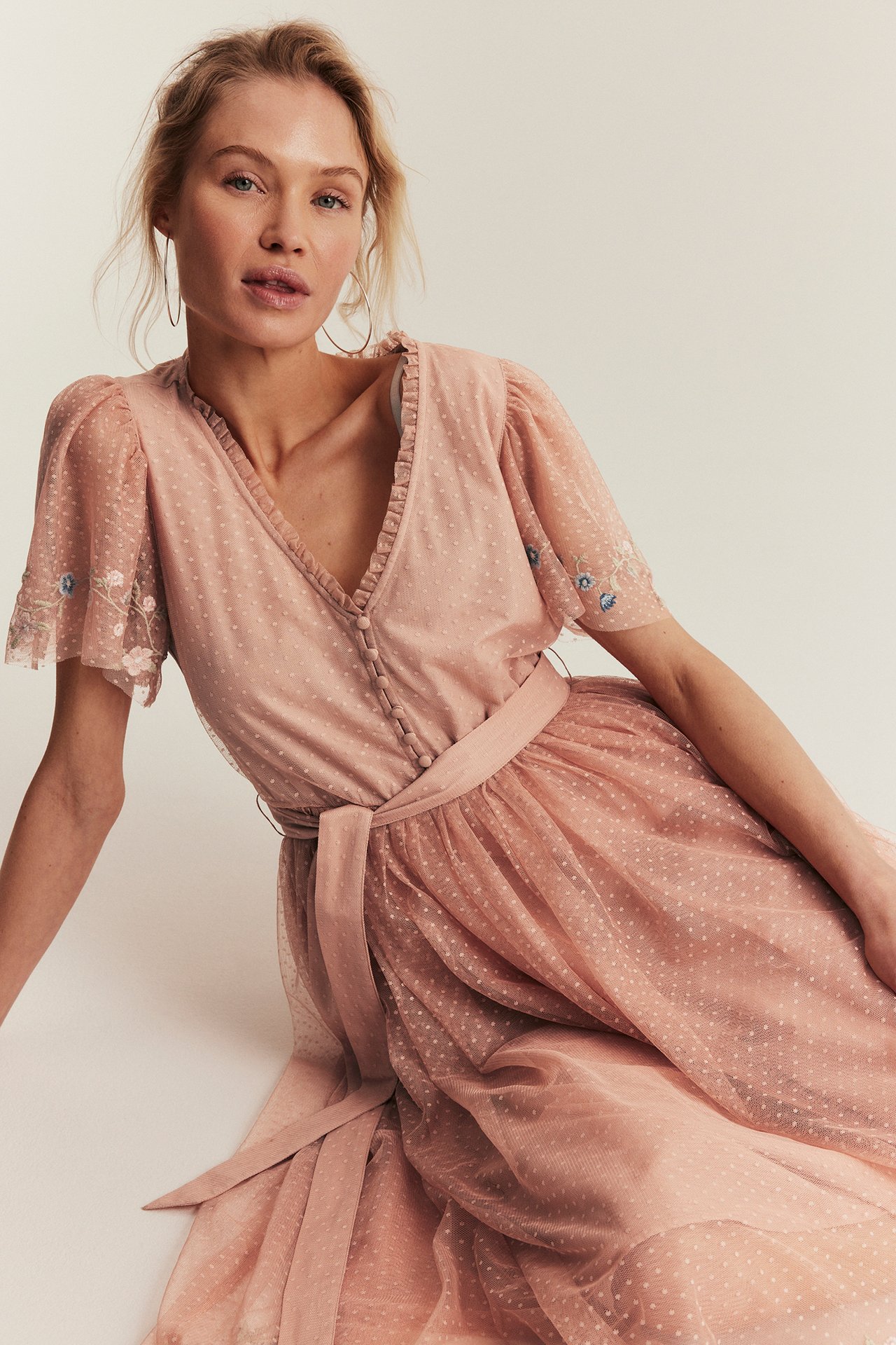 Front view: Woman in a pink dotted mesh dress with embroidered short sleeves and a tie belt.