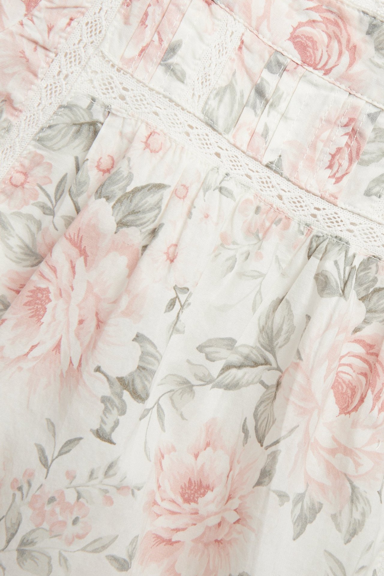 Nahaufnahme des cremeweißen Blumenstoffes mit rosa Rosen, grauen Blättern, Spitzeneinsätzen und Abnähern.