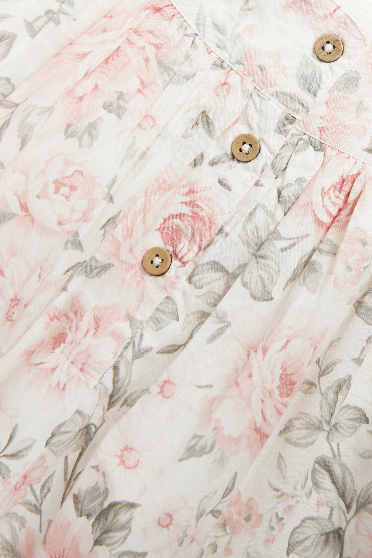 Close-up of an off-white floral cotton dress with pink roses, green leaves, and three wooden buttons.