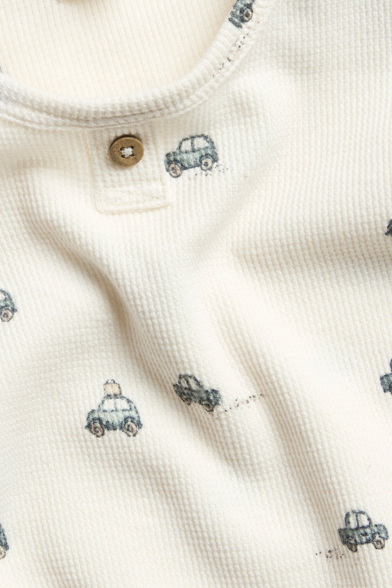 Offwhite Langarmbody aus Flauschstoff mit Auto-Motiv, Knopf vorn, Druckknöpfe in der Schrittnaht.