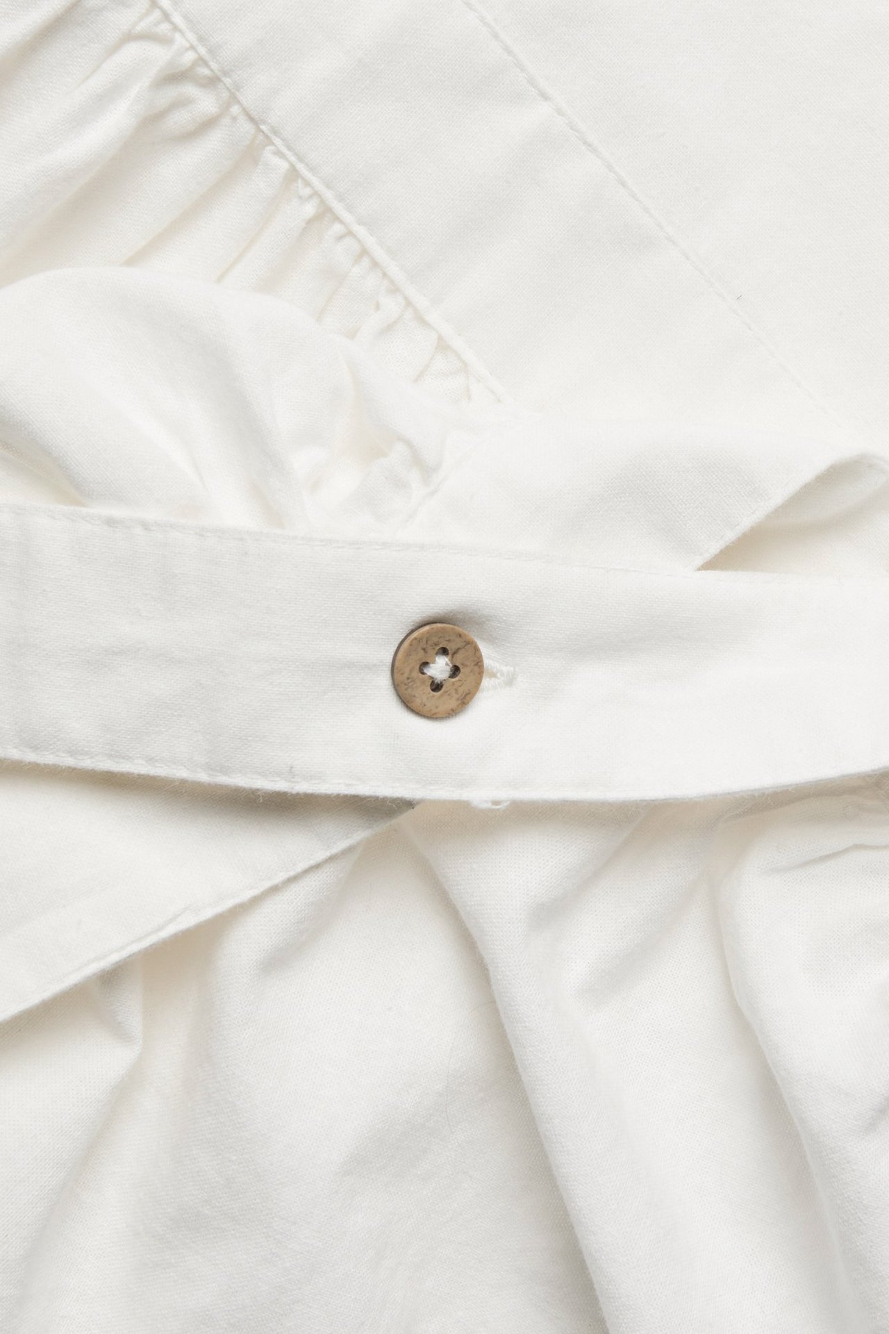 Close-up of an off-white cotton apron with ruffles and a wooden button on a strap.