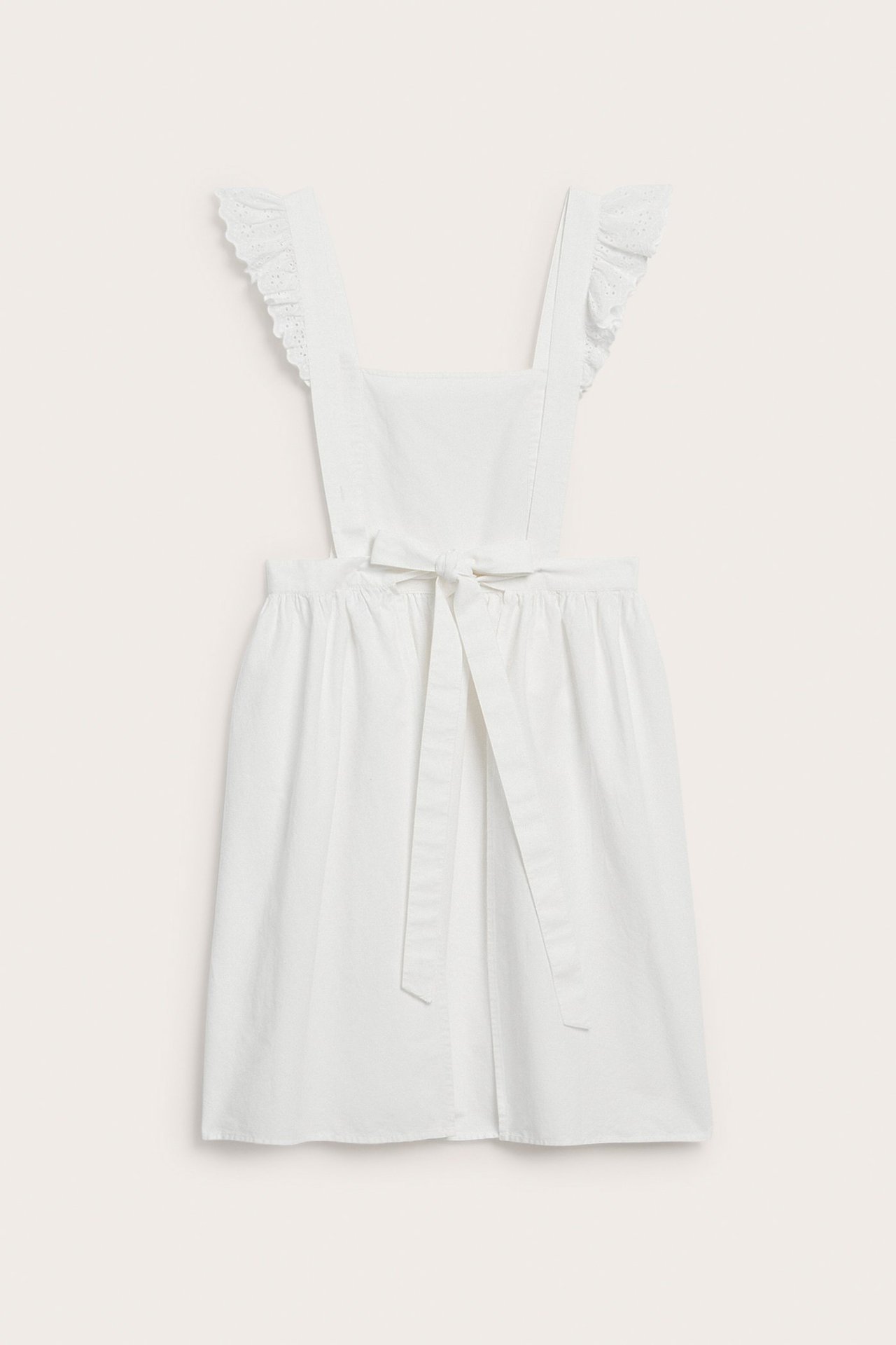 Front view of an off-white cotton apron with ruffled straps and a tied bow at the waist.