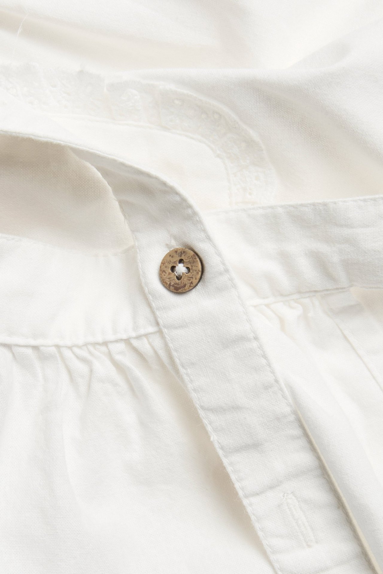 Close-up of an off-white cotton kid's apron with a brown wooden button and delicate lace trim.