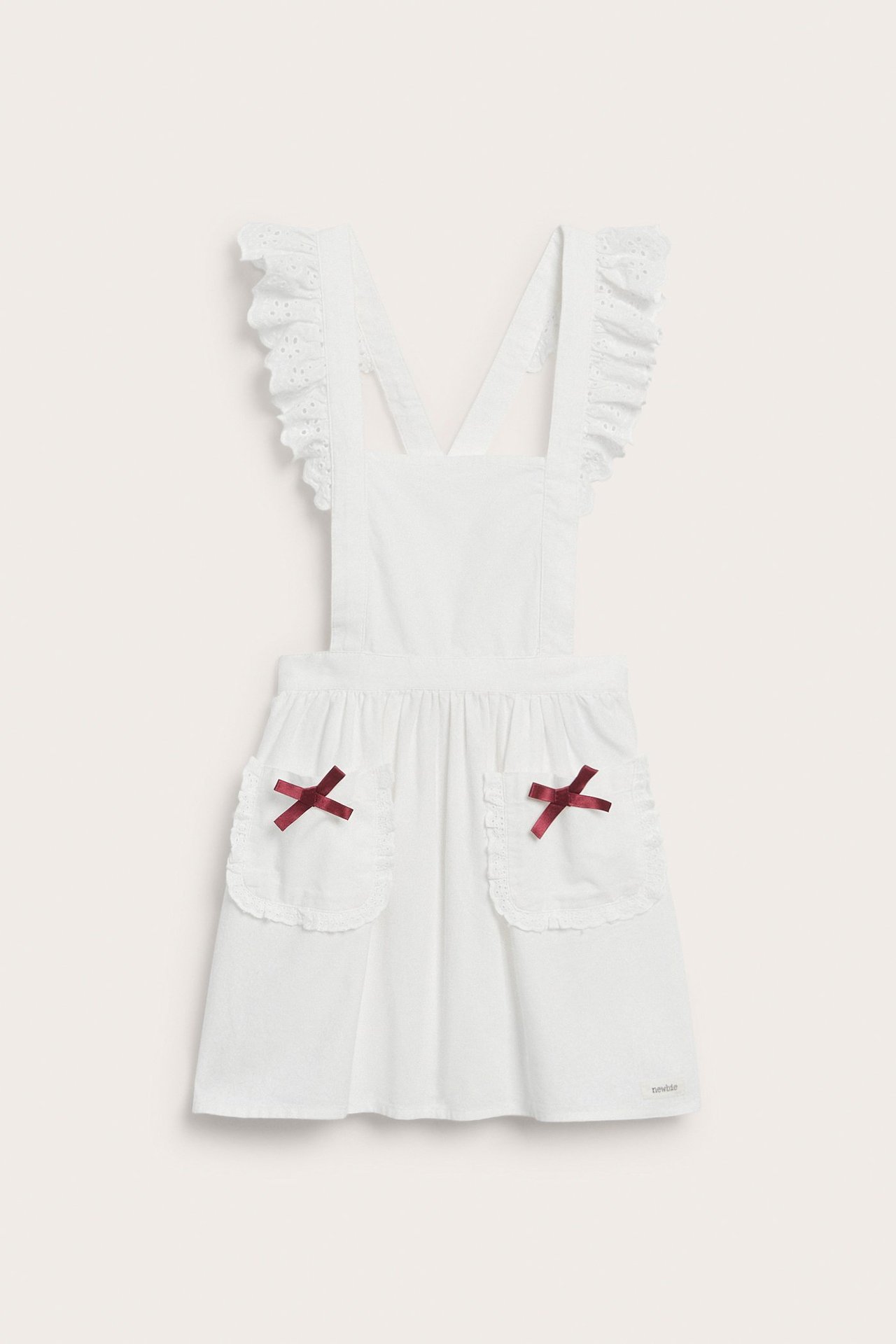 Front view: Kid's off-white cotton apron with ruffles on straps and red bows on two front pockets.