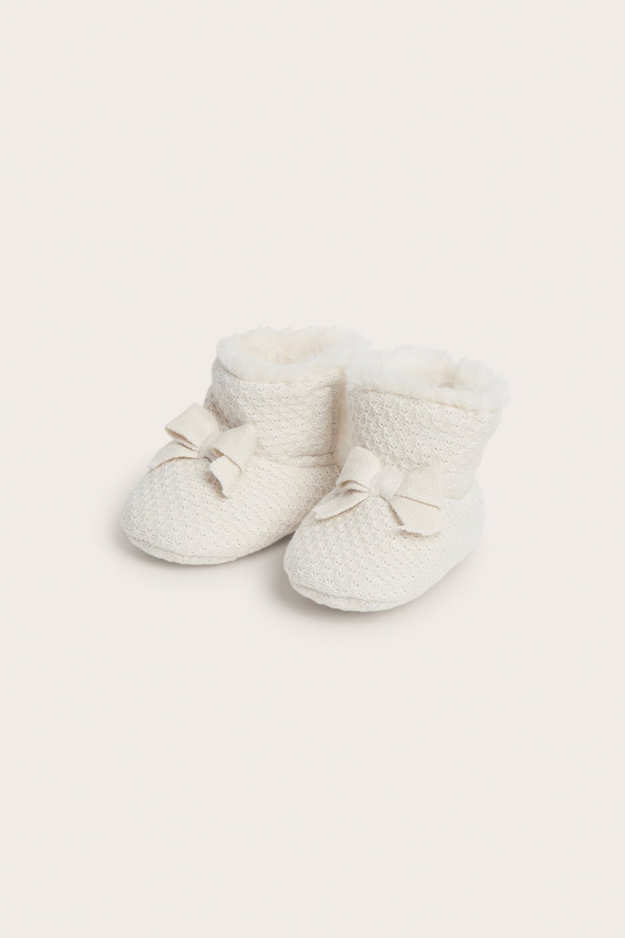 Front view of off-white knitted baby booties with soft lining and small bows.