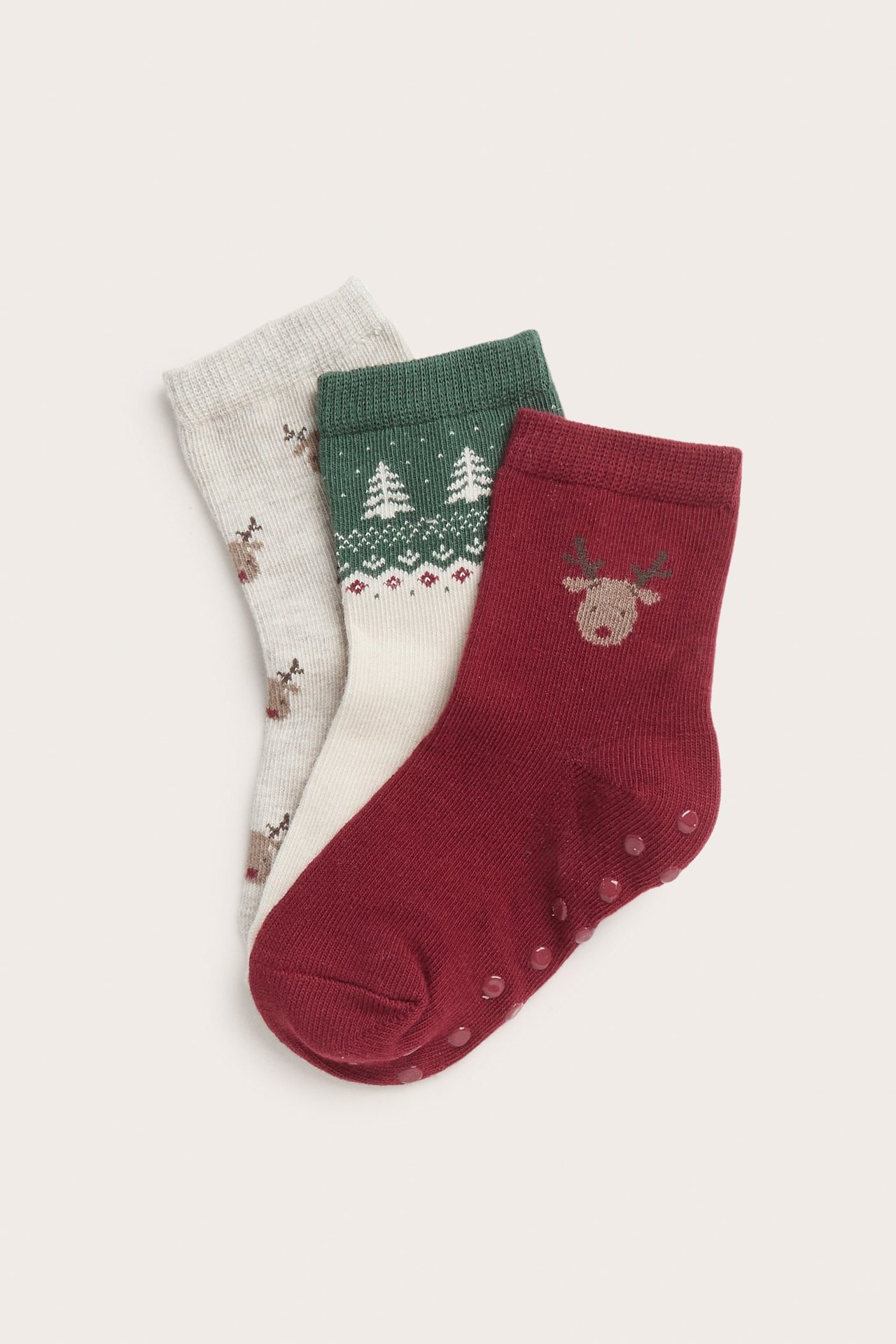 Close-up: Three pairs of kids' anti-slip knitted socks; red reindeer, cream Christmas tree, and grey reindeer pattern.