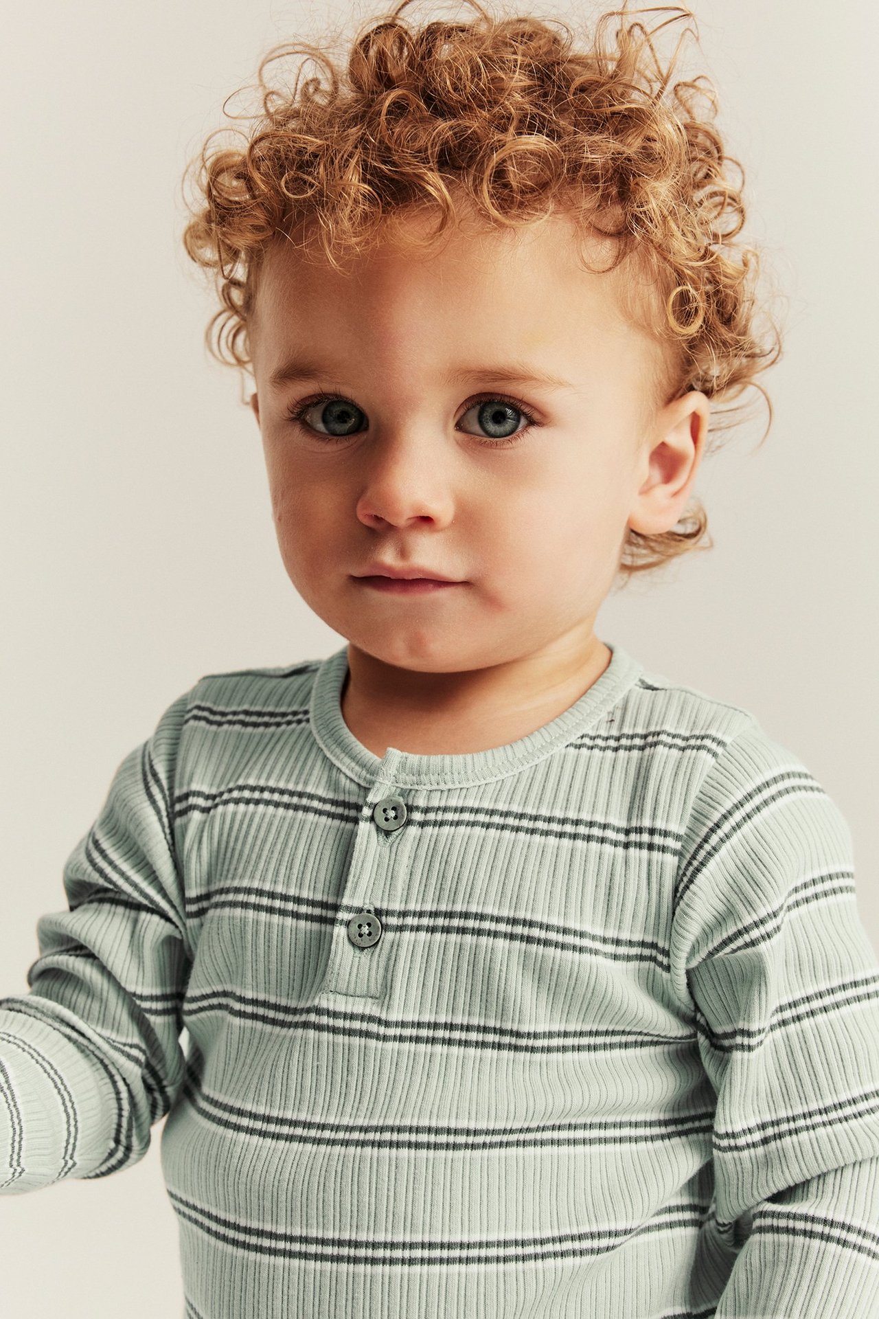 Close-up, front view of a baby wearing a light green ribbed long-sleeved bodysuit with dark stripes and front buttons.