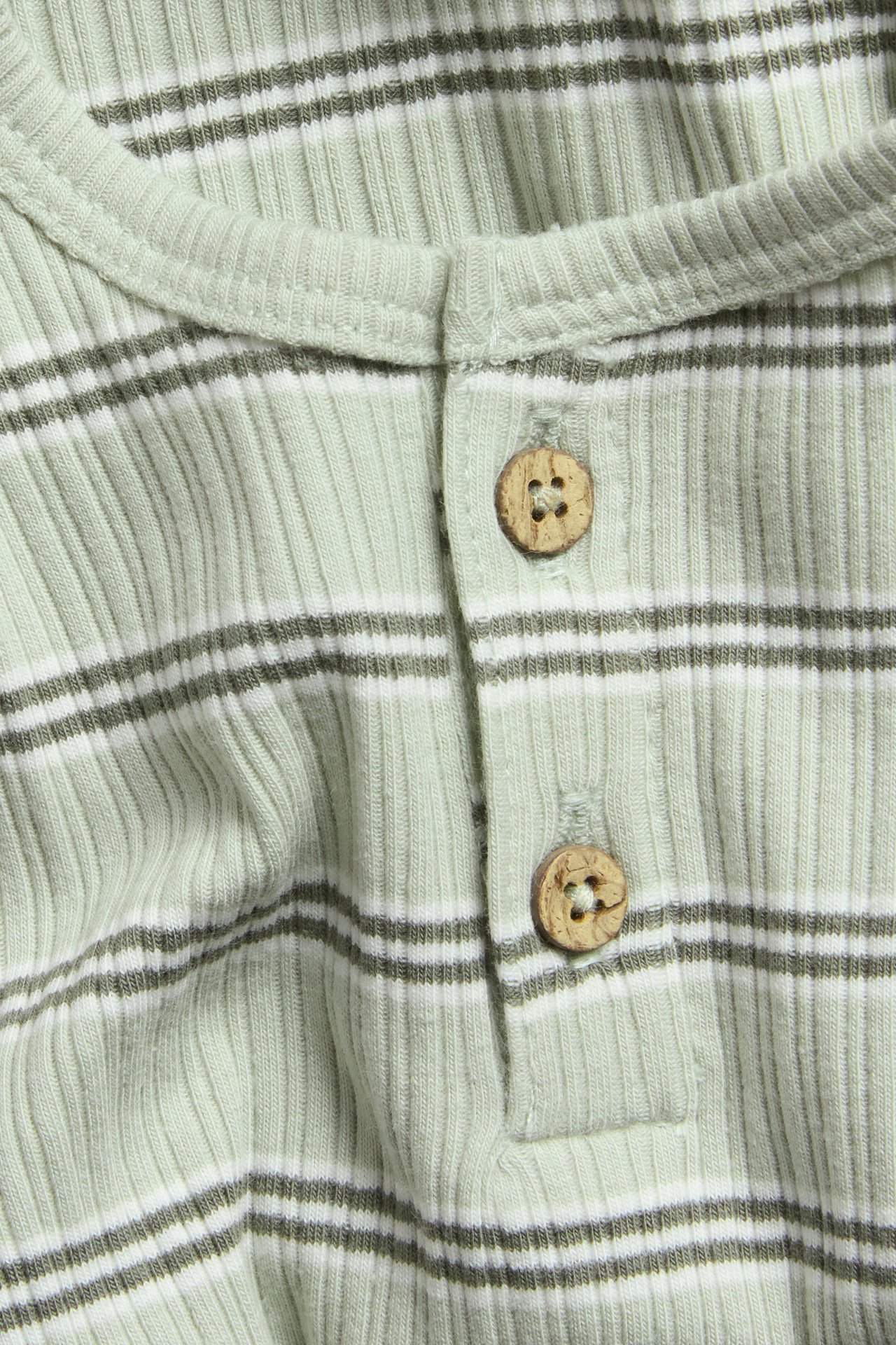 Close-up: Light green ribbed baby bodysuit with dark green and white stripes, featuring two wooden buttons.