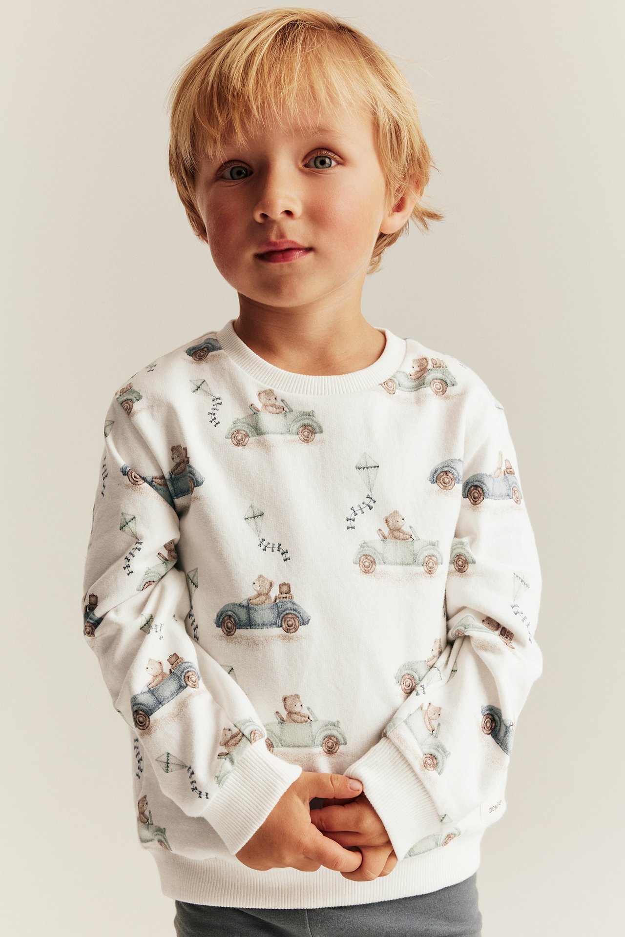 Front view, boy wearing an off-white cotton sweatshirt with car and bear pattern.