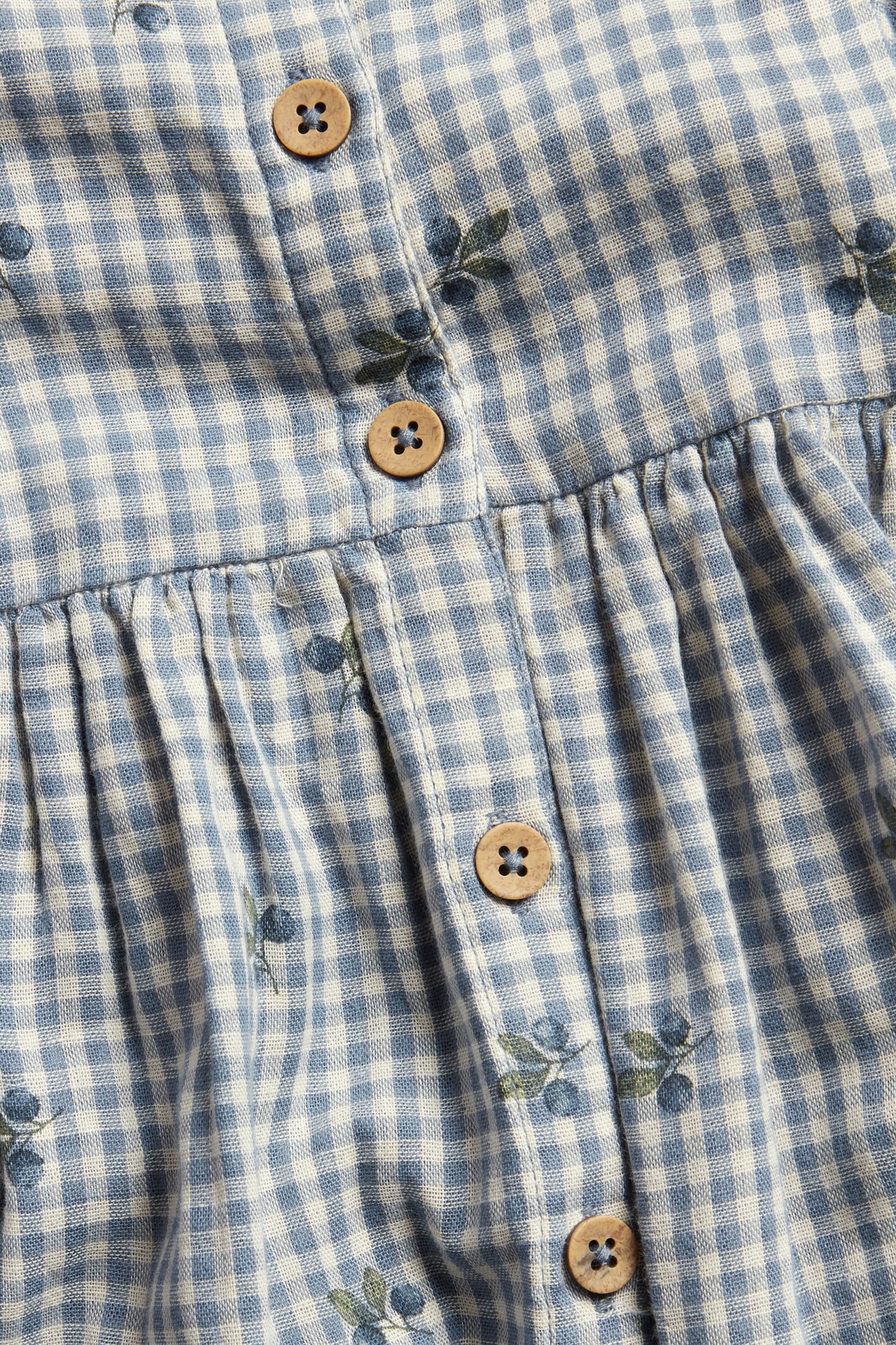 Close-up of a blue and white checkered dress with a blueberry print, wooden buttons, and gathered fabric.