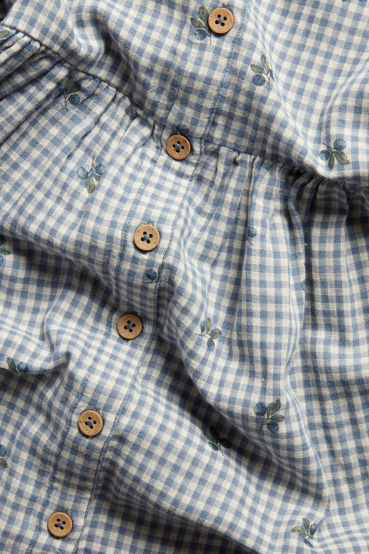 Nahaufnahme eines blau-weiß karierten Baumwollkleides mit Blaubeerprint und sichtbaren Holzknöpfen.