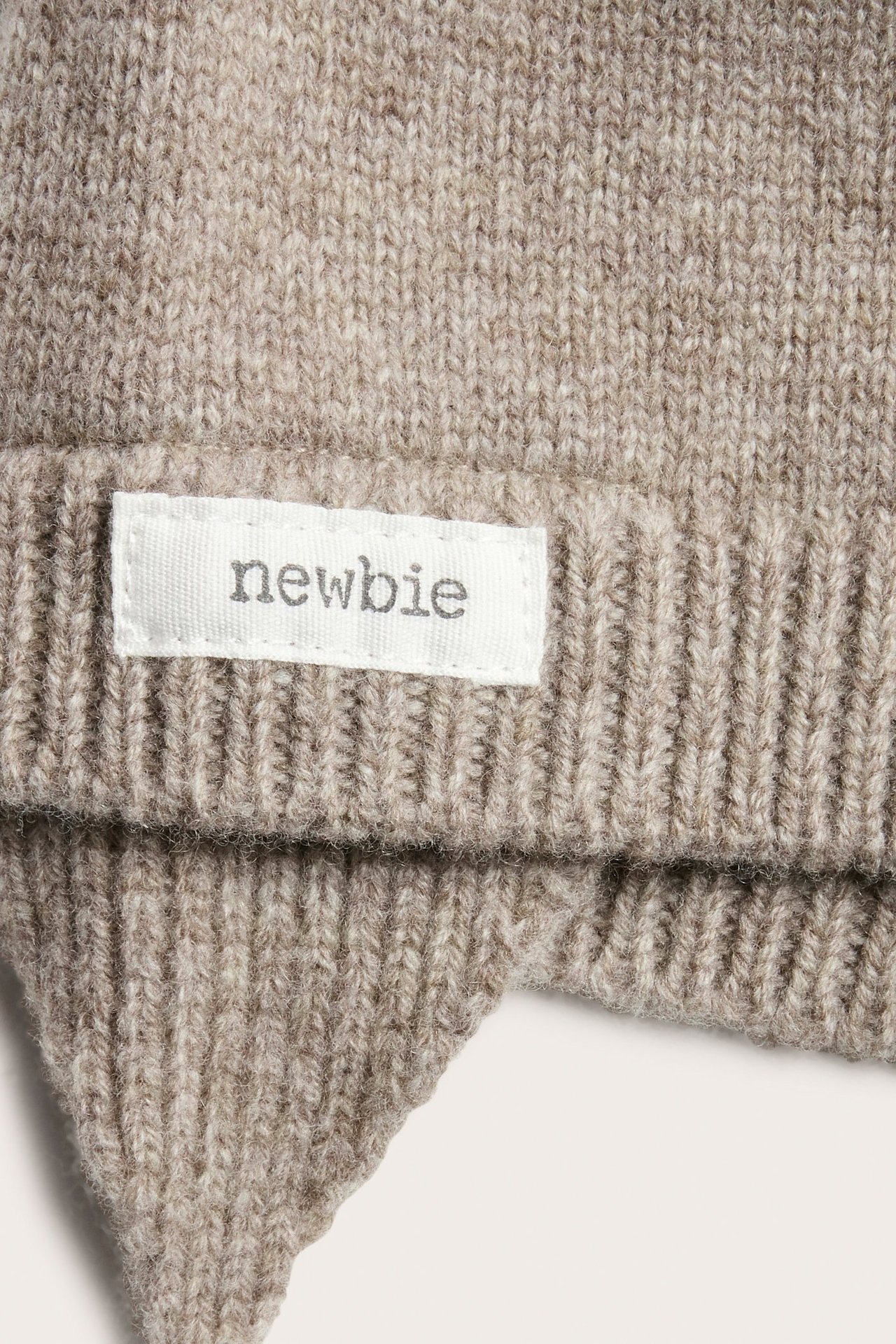 Nahaufnahme einer melierten braunen Baby-Wollmütze mit Ohrenklappen und weißem Etikett.