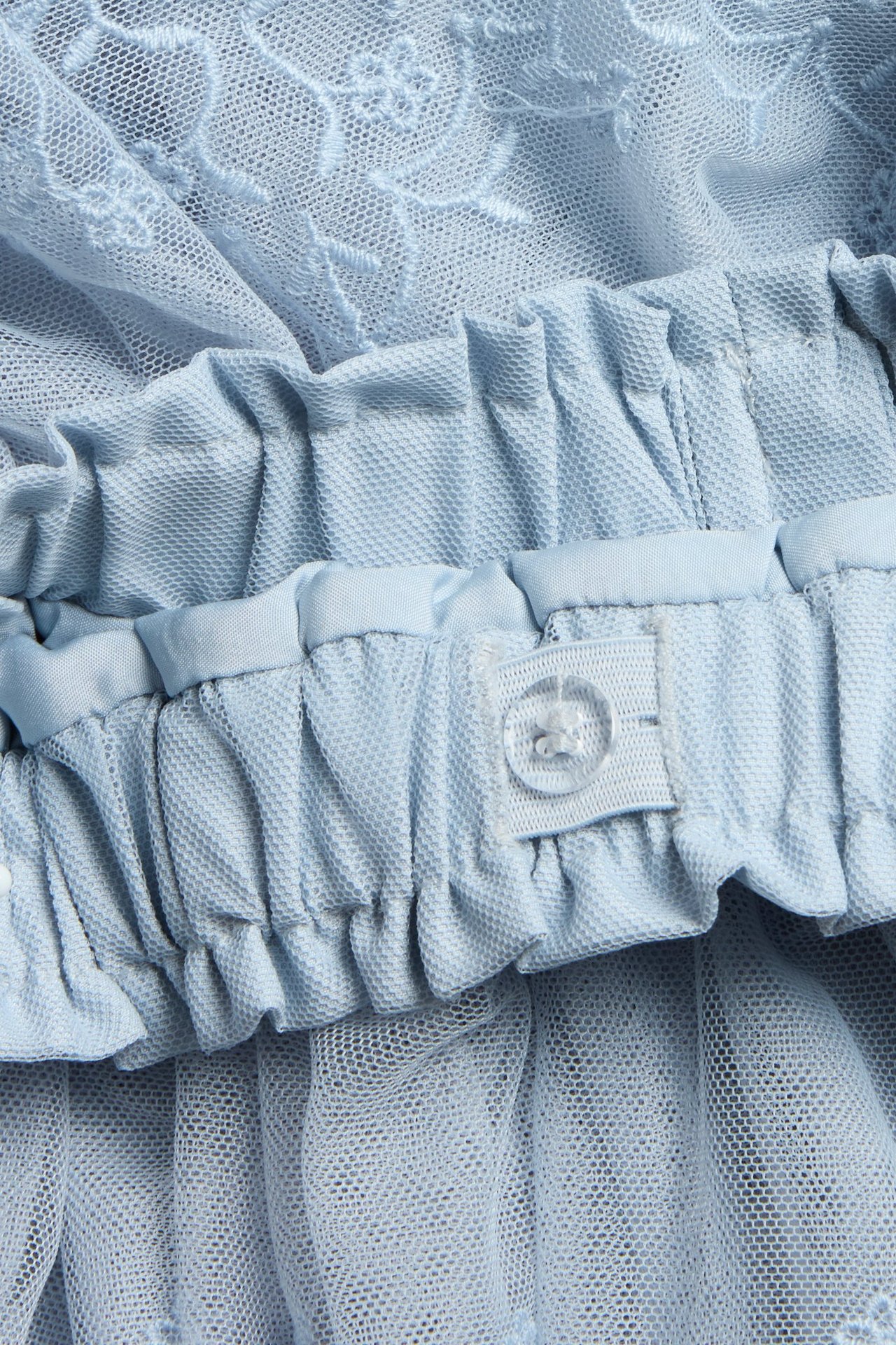 Close-up of a kid's blue embroidered mesh skirt with ruffles and an adjustable elastic waistband.