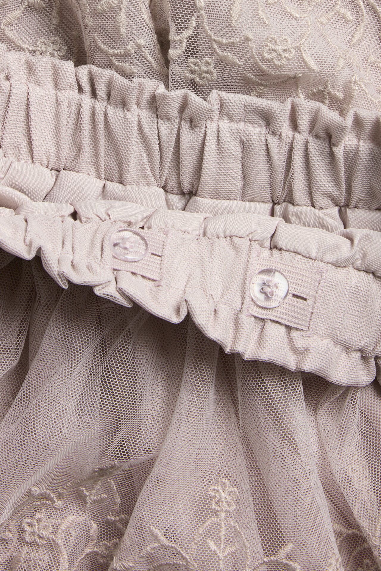 Close-up of light lilac embroidered mesh skirt with ruffled, adjustable elastic waistband and buttons.
