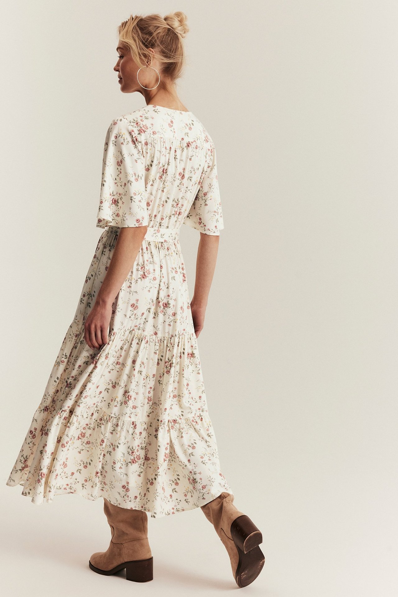 Seitenansicht einer Frau in einem cremefarbenen floralen, gestuften Viskose-Maxikleid und hellbraunen Stiefeln.