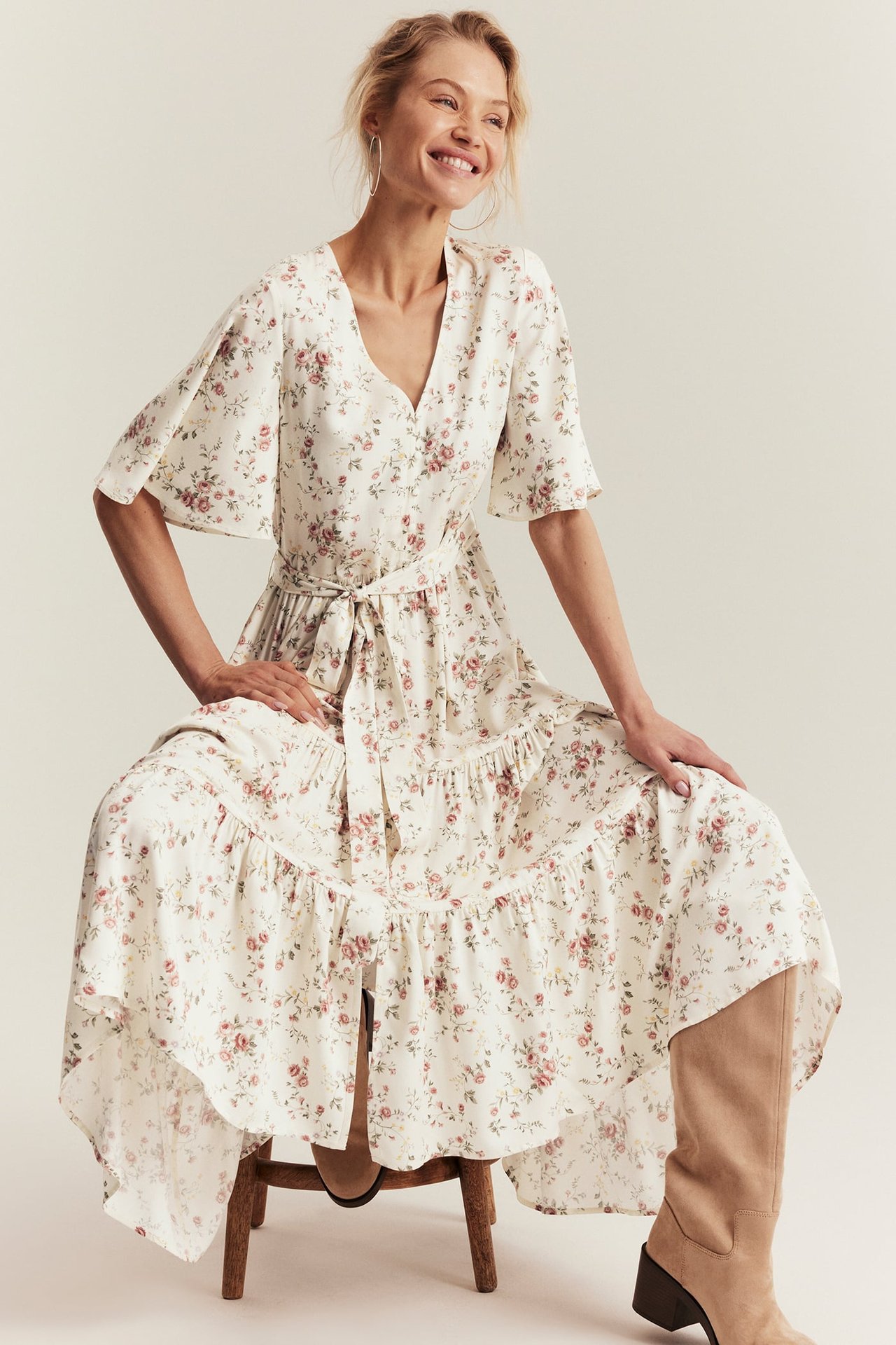 Front view of a woman wearing an off-white floral viscose tiered dress with a tied belt and beige boots.