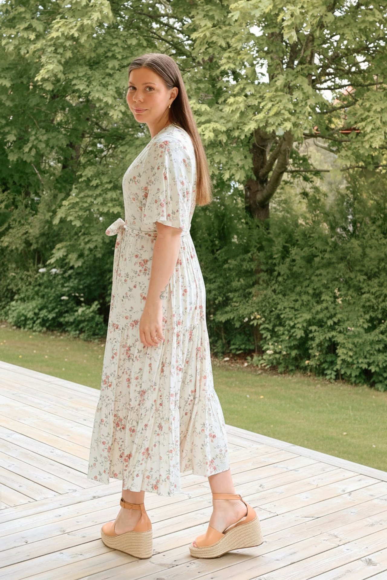 Side view of woman in offwhite floral viscose midi dress with tied belt and tan wedge sandals.