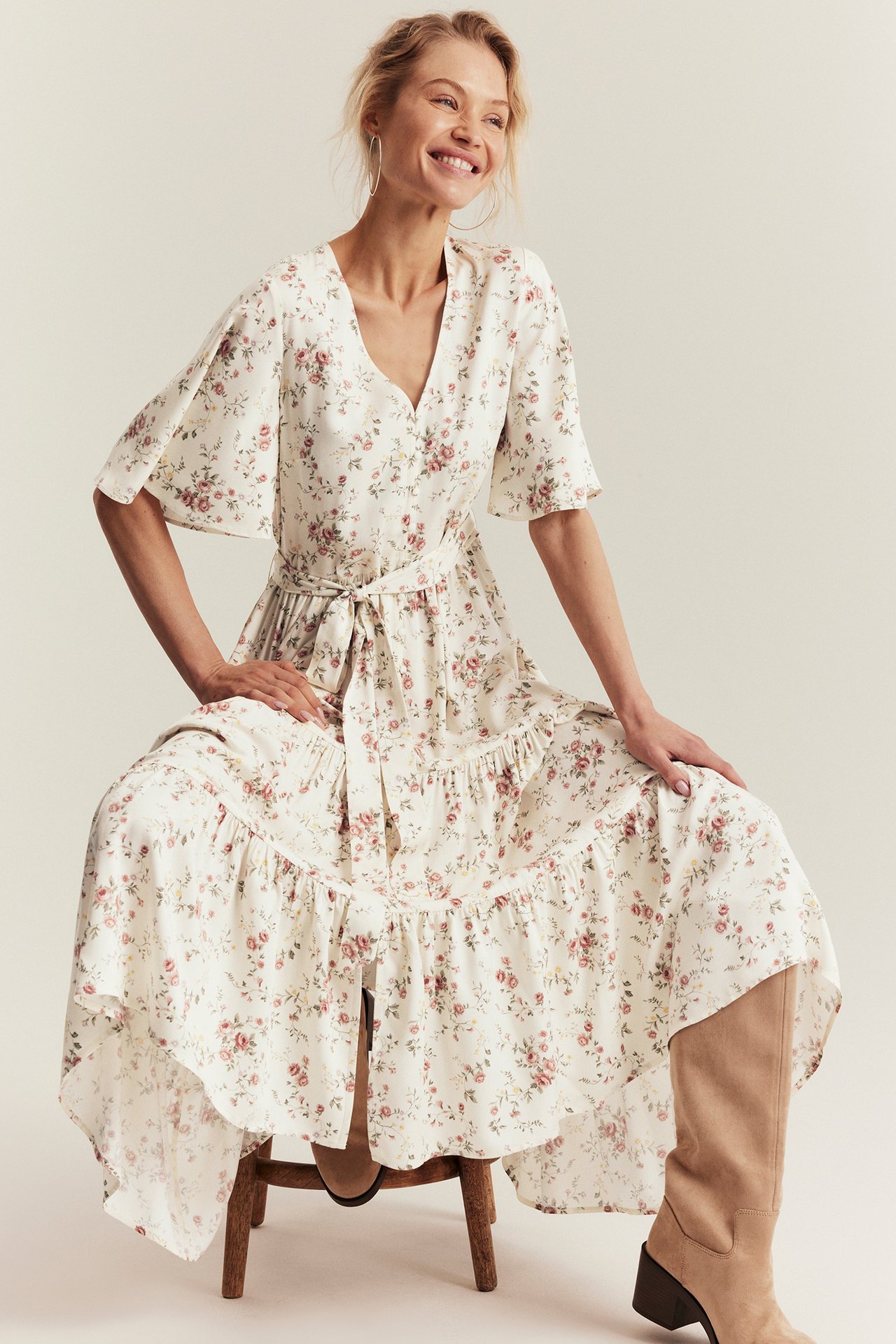Front view of woman in off-white floral V-neck viscose dress with tie belt and beige boots.
