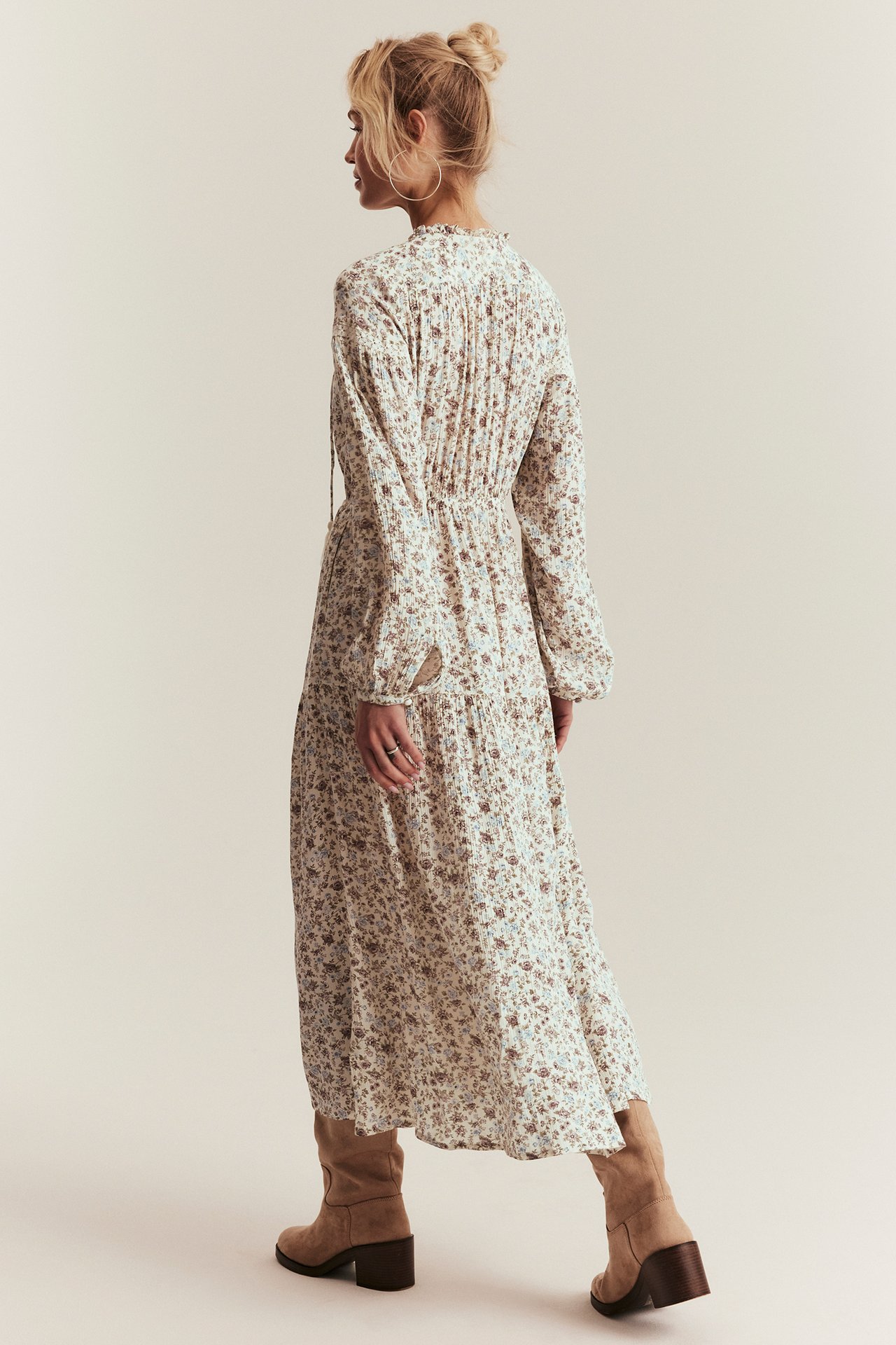Back-side view: Woman in a long offwhite floral viscose dress with puff sleeves and beige boots.