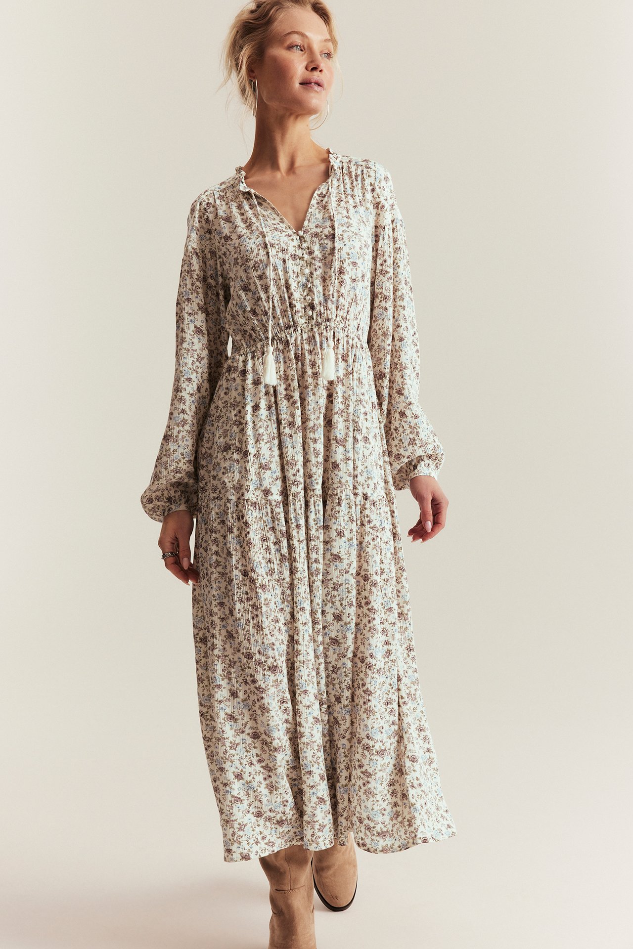 Front view: Woman in an off-white floral dress with a ruffled V-neck, tie-bands, elastic waist.