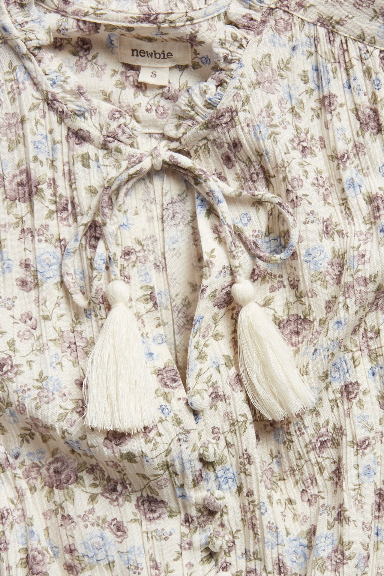 Close-up of off-white floral viscose dress with ruffled collar, tassel ties, and front buttons.
