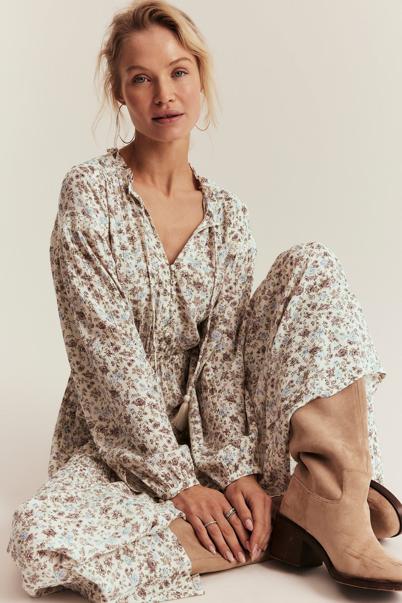Front view, woman in an off-white floral viscose maxi dress with ruffle collar, tie-bands, and beige suede boots.