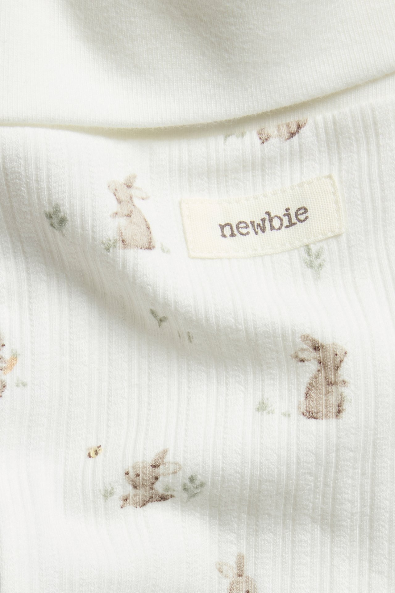 Close-up of offwhite ribbed leggings with a bunny print and a cream-colored label.