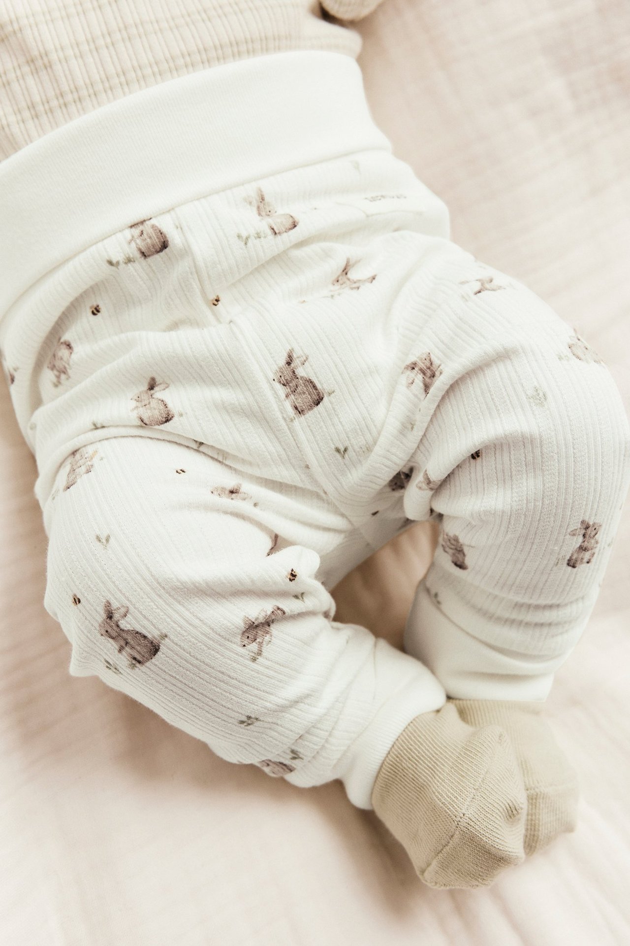 Nahaufnahme eines Babys in cremeweißen Ripp-Leggings mit Kaninchendruck und hellbeigen Socken.