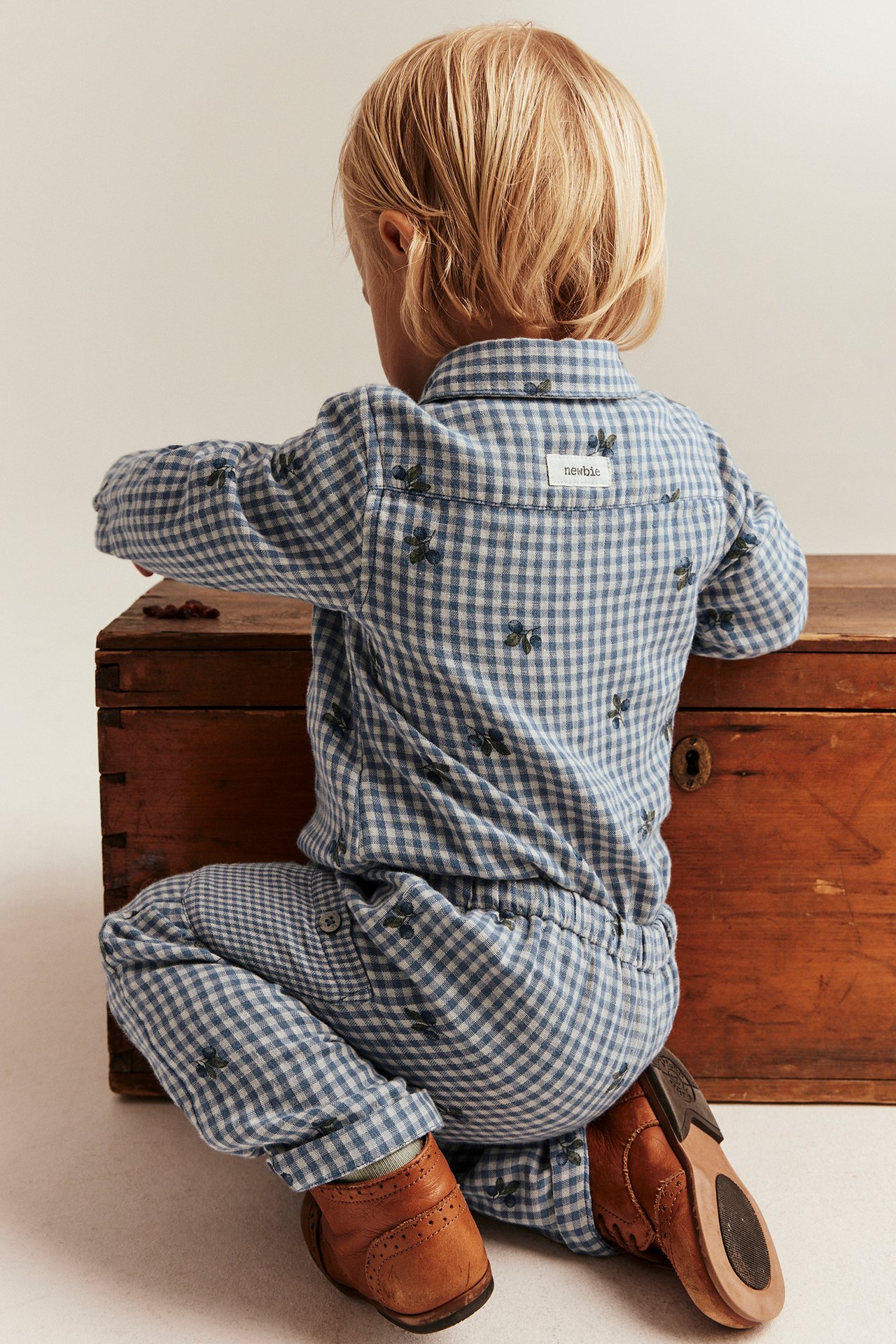 Rückansicht eines Kindes in blau kariertem Baumwoll-Shirt-Body mit Blaubeerprint und braunen Schuhen.