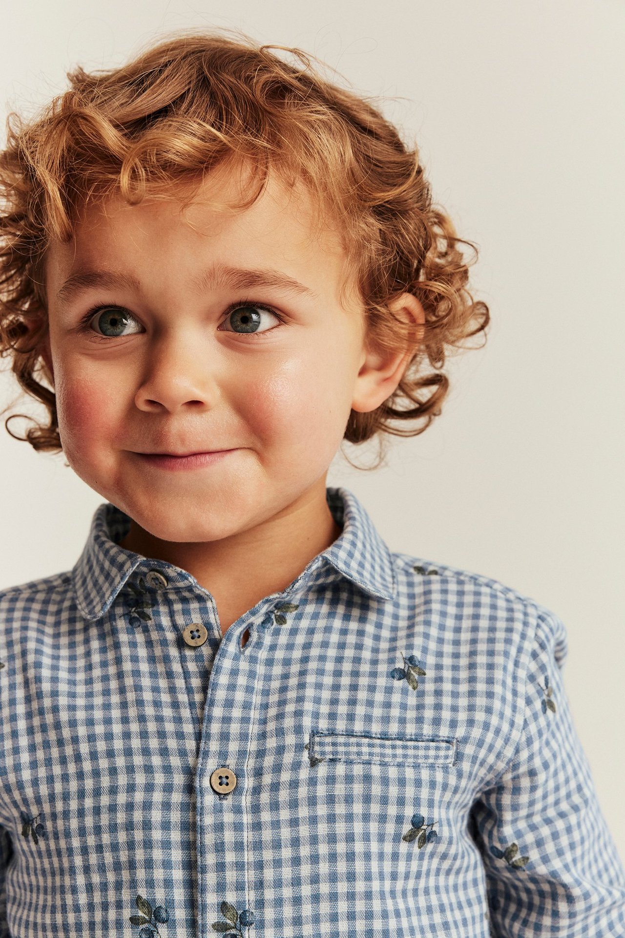 Close-up front view: Kid wears a blue checked cotton shirt with blueberry print, collar, and chest pocket.